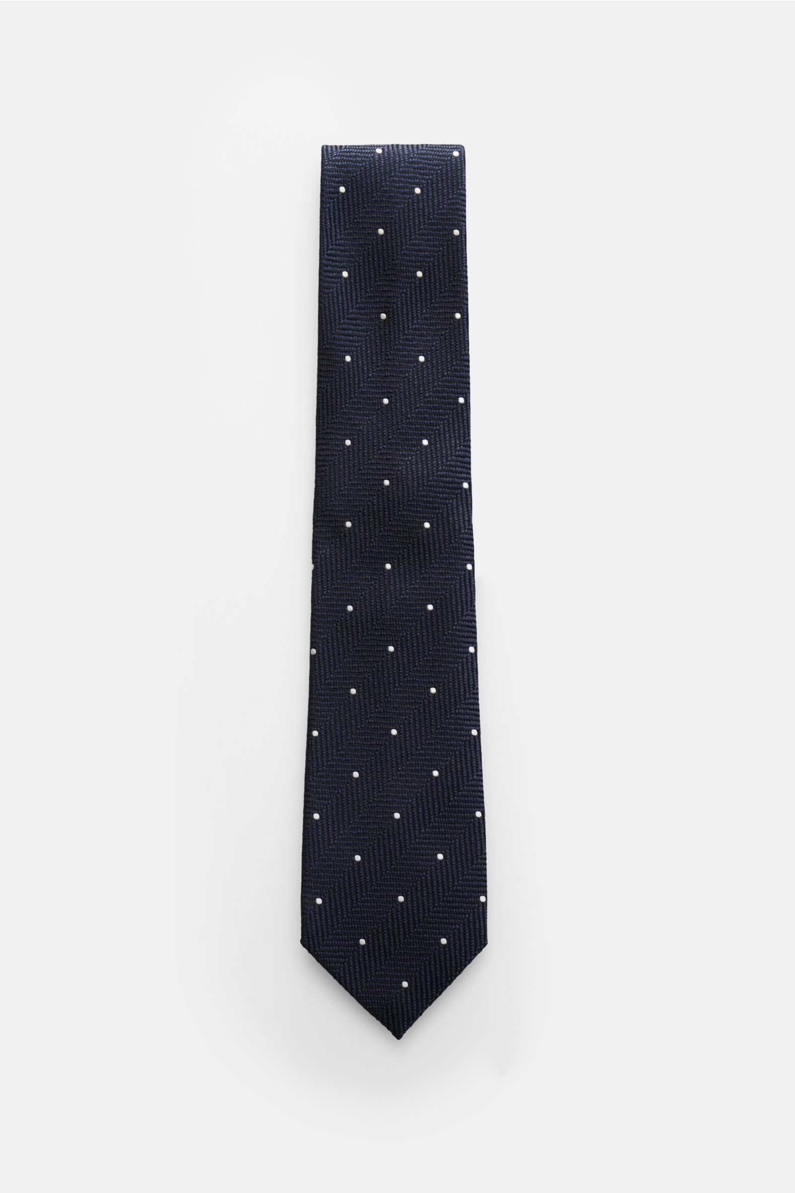 Top-down view of the Tom Ford Seidenkrawatte navy/schwarz/creme gemustert tie, showcasing a navy silk fabric with a subtle sheen, timeless herringbone pattern with cream dots, logo stitching, made in Italy, width 8 cm. Souveräne Eleganz bis ins Detail: Di
