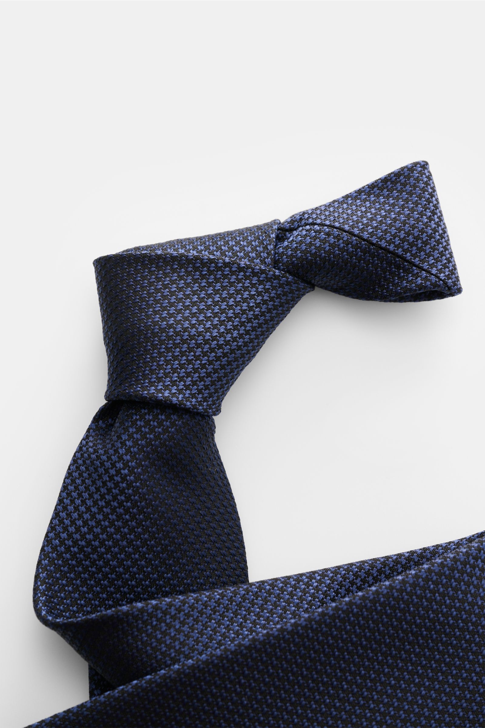 Tom Ford Seidenkrawatte dunkelblau/schwarz gemustert, Hahnentrittmuster, Seide, dezenter Glanz, Logo-Stitching, Detailfoto von oben, made in Italy.