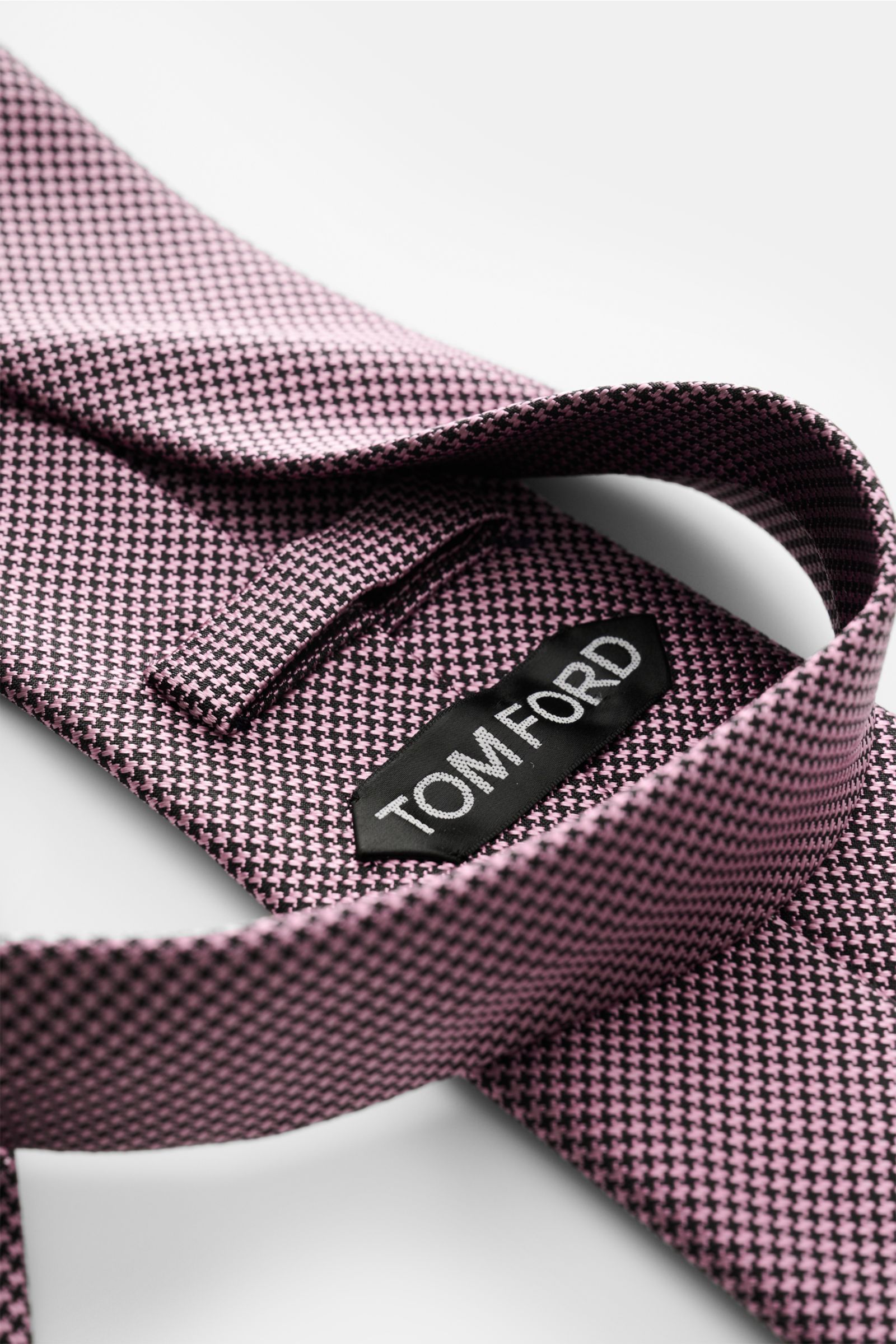 Tom Ford Seidenkrawatte rosé/schwarz gemustert mit Hahnentritt, Logo-Stitching, reine Seide, dezenter Glanz, seitliche Nahaufnahme.