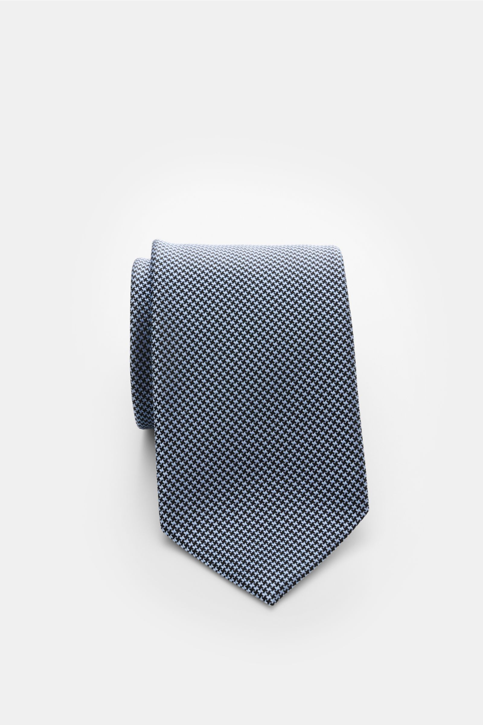 Tom Ford Seidenkrawatte hellblau/schwarz gemustert, Nahaufnahme von oben, reine Seide, dezenter Glanz, Hahnentrittmuster, Logo-Stitching, 8 cm breit, made in Italy.