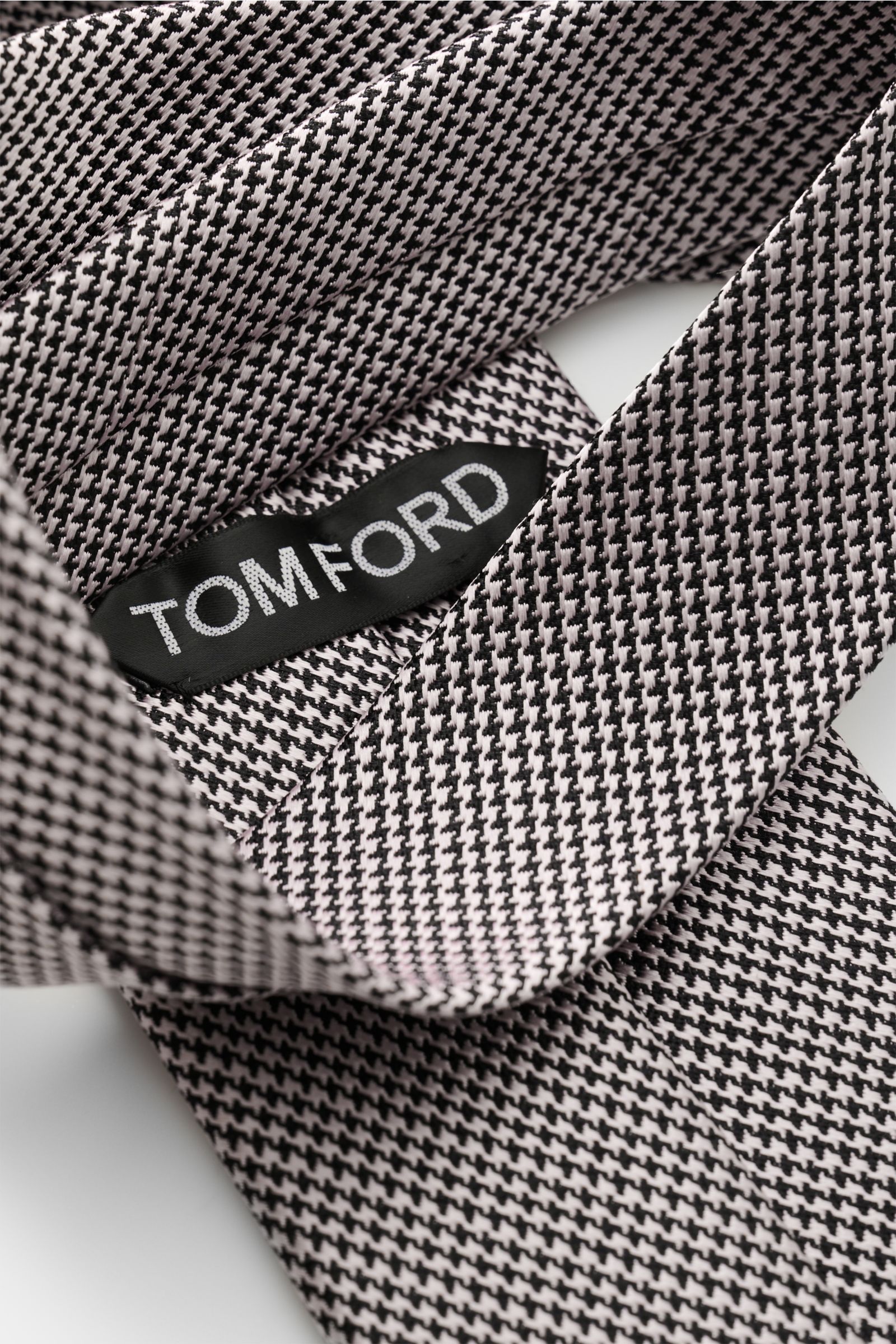 Tom Ford Seidenkrawatte rosé/schwarz gemustert mit Hahnentrittmuster, Logo-Stitching, reine Seide, dezenter Glanz, Nahaufnahme von oben.