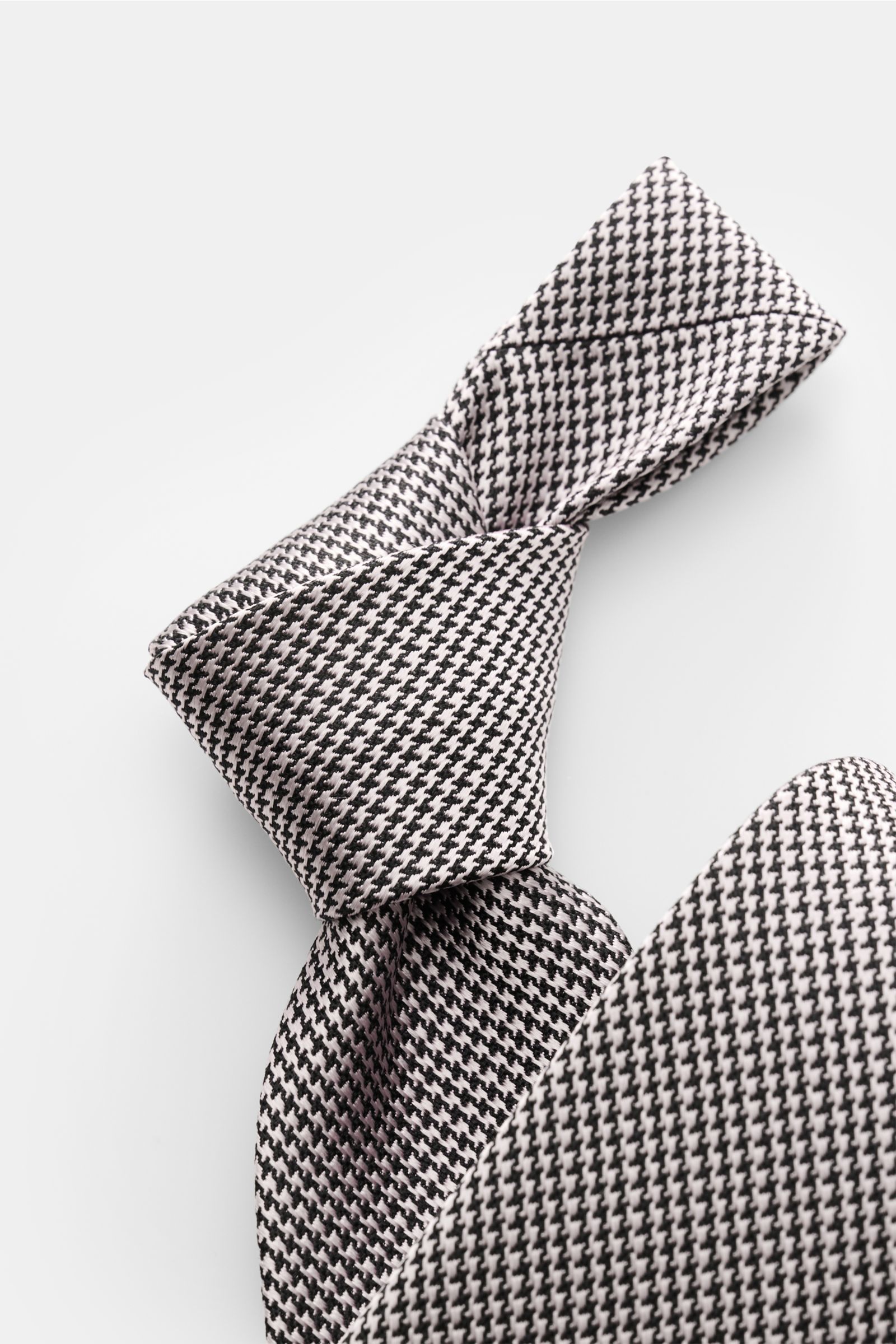 Tom Ford Seidenkrawatte rosé/schwarz gemustert mit Hahnentritt, reine Seide, dezenter Glanz, Logo-Stitching, made in Italy, 8 cm breit, Nahaufnahme von schräger Perspektive.