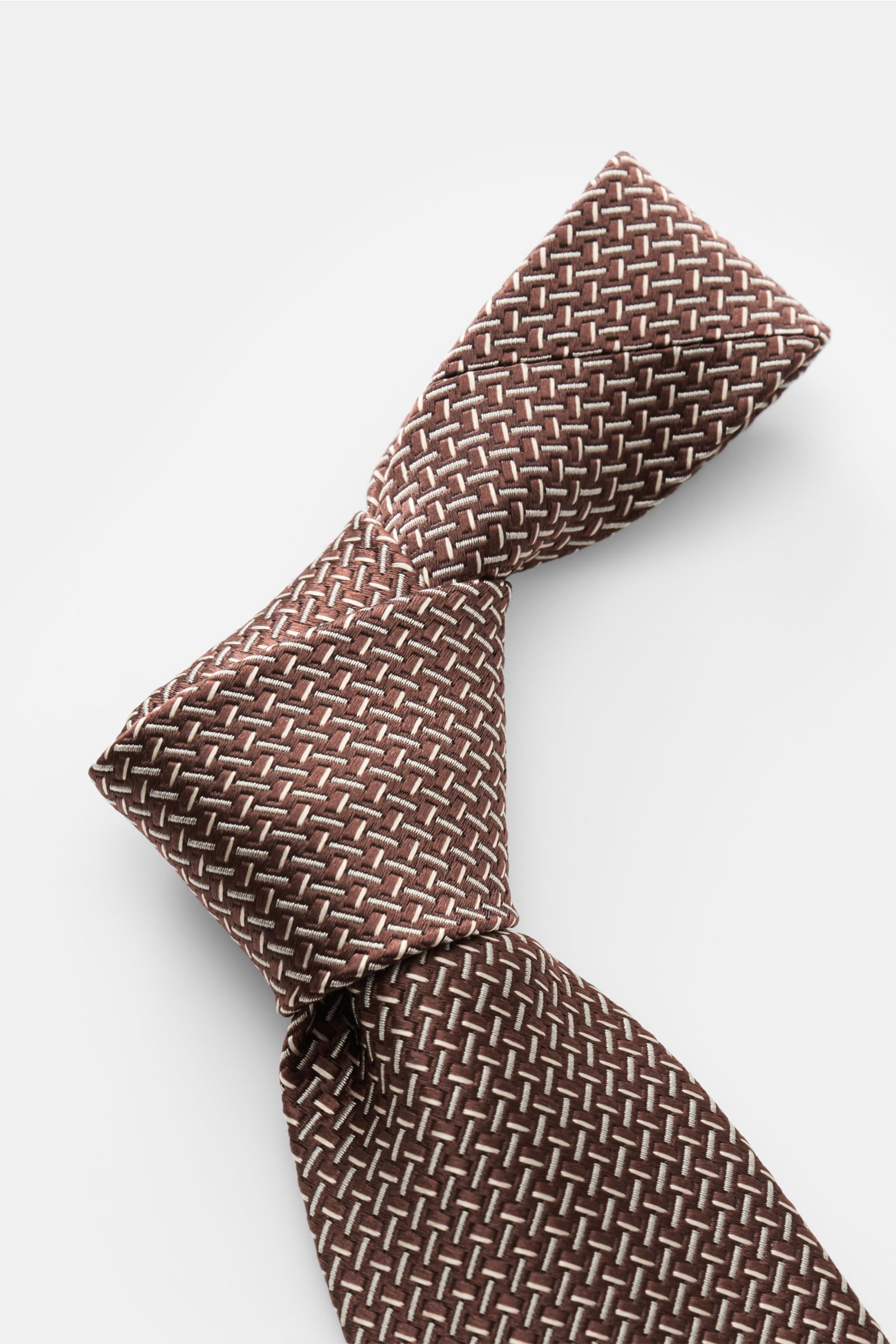 Tom Ford Seidenkrawatte braun/creme gemustert, Nahaufnahme aus schräger Perspektive, reine Seide, dezenter Glanz, Logo-Stitching, 8 cm breit, made in Italy.