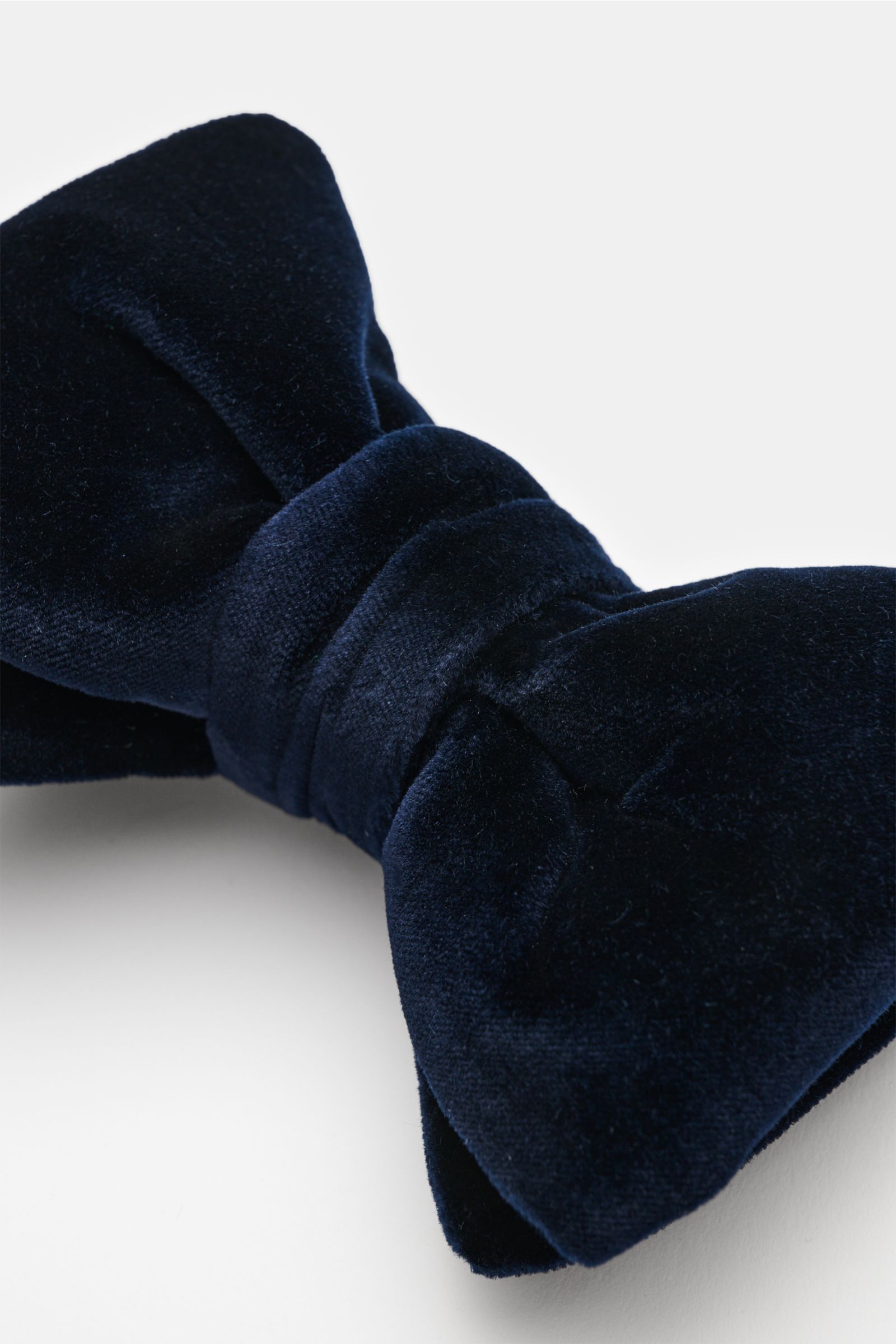 Close-up front-angle view of a Tom Ford Samt-Schleife dunkelblau, showing a dark blue velvet bow tie made of Samt aus Viskose und Cupro, with weicher Griff, materialtypische Optik, gebundene Ausführung, and Made in Italy.