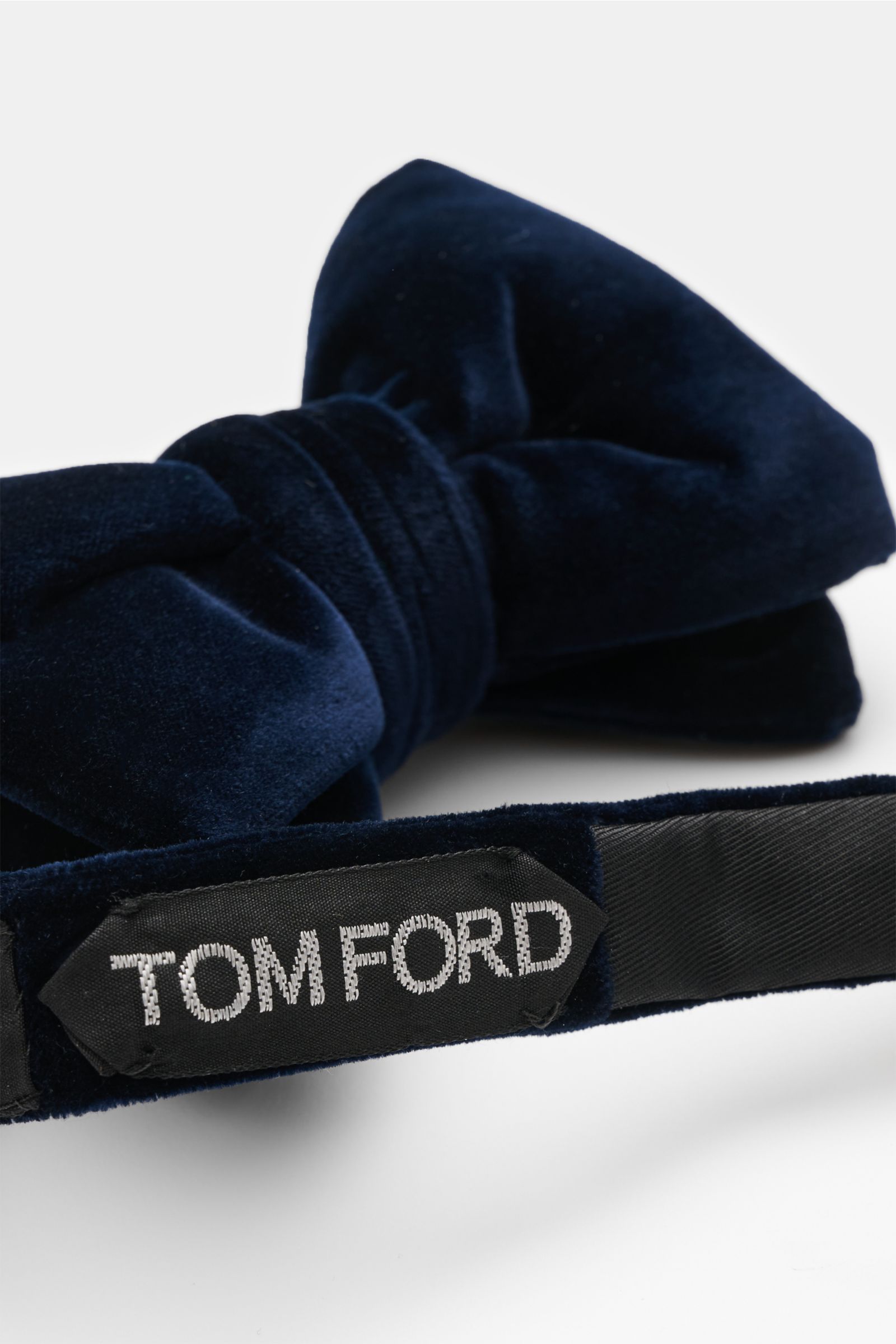 Close-up front-side view of the Tom Ford Samt-Schleife dunkelblau, a dark blue velvet bow tie with a soft grip, made from viscose and cupro, featuring material-typical texture, tied design, and Made in Italy label.