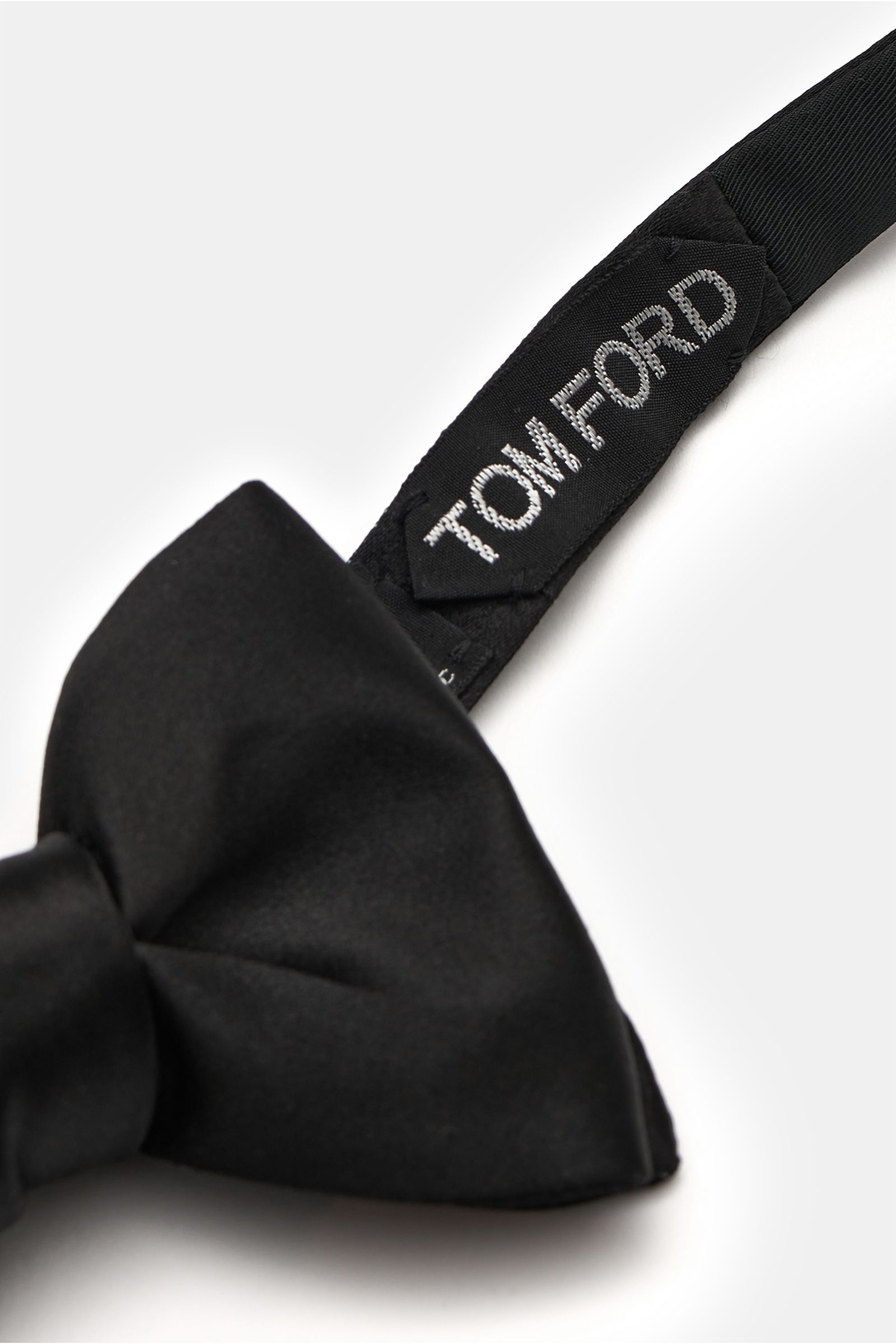 Front close-up of a Tom Ford Seidenschleife schwarz, an elegant black silk satin bow tie with slight sheen, tied style, approx. 10.5 cm wide, showing the stitched Tom Ford label on the strap.

Diese elegante gebundene Schleife von TOM FORD besteht aus 
