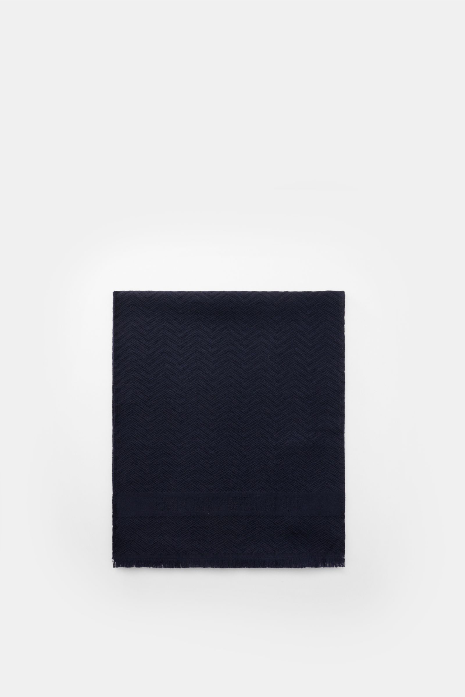 Emporio Armani Schal navy folded flat, photographed from above, showing tonal herringbone wool fabric, soft texture, logo stripe, and narrow fringed edge. Italienische Eleganz für jeden Tag: Der edle Schal von EMPORIO ARMANI aus reiner Wolle überzeugt mit