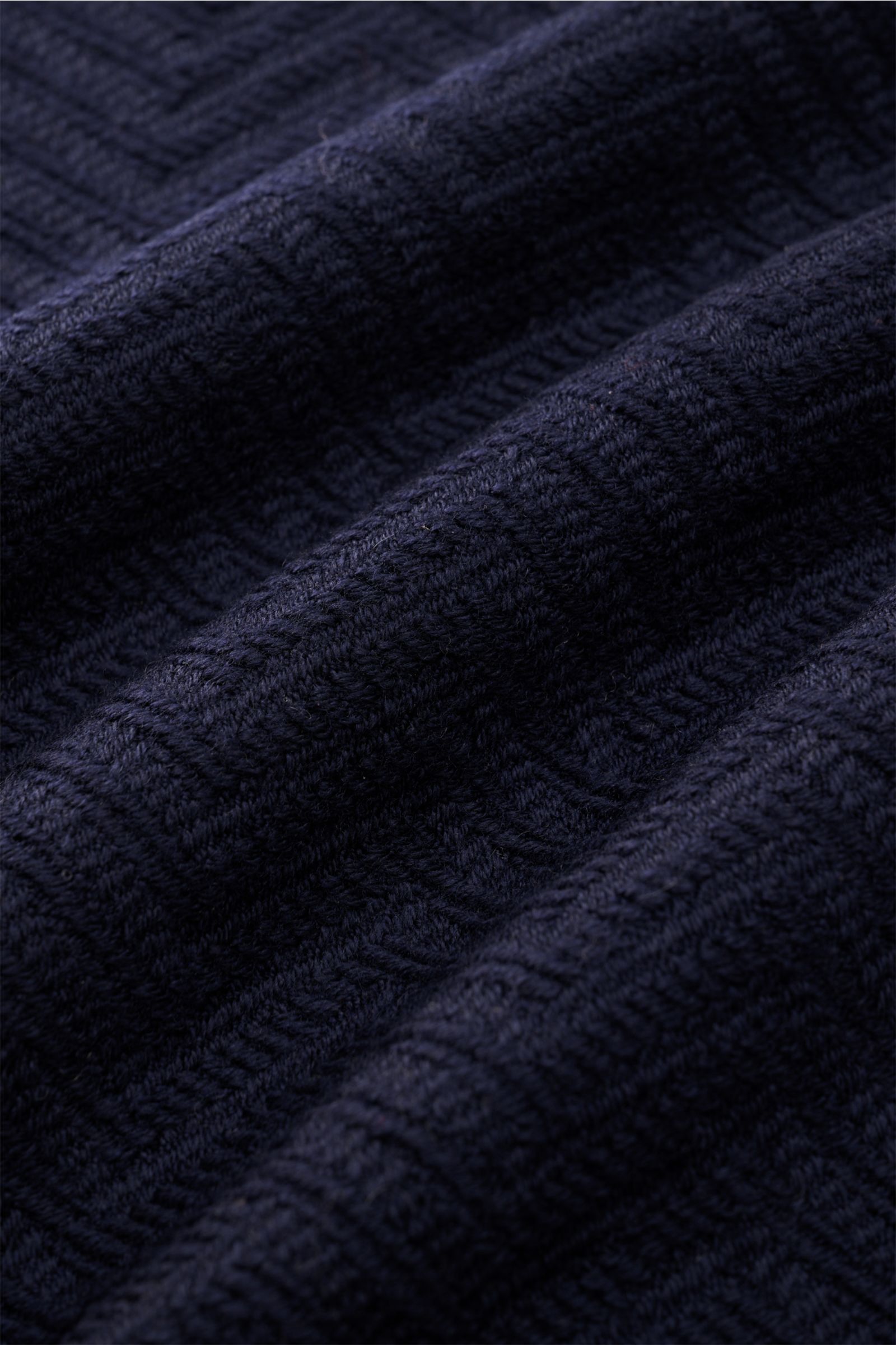 Close-up, angled view of the Emporio Armani Schal navy showing its soft, textured pure wool fabric with tonal herringbone weave and subtle logo stripe. Italian elegance for everyday wear with a narrow fringed edge, measuring approximately 175 cm by 37.5 c