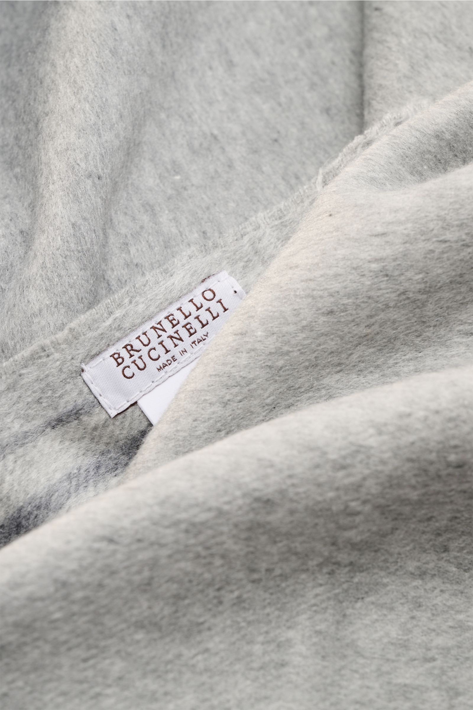 Close-up image of the Brunello Cucinelli Seidenschal navy/grau/bordeaux showing a soft fabric surface and the sewn-in label from a top-front angle; reine Seide, sehr weicher Griff, schmale Kontraststreifen, Saum mit Fransen, Maße: ca. 155 cm x 48 cm.