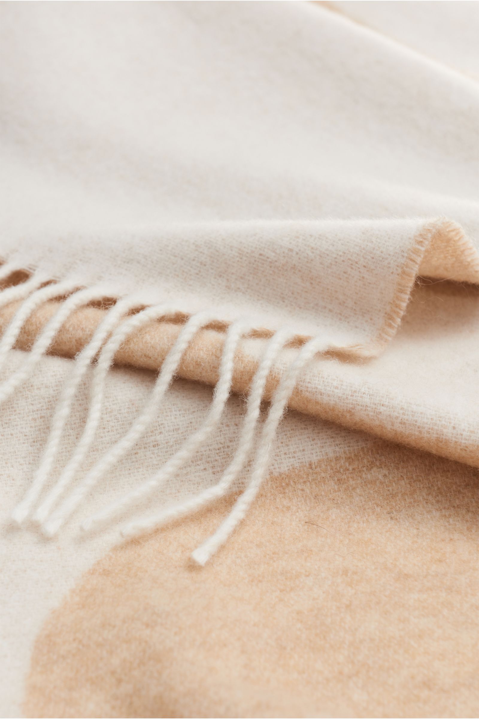 Close-up image of the A.P.C. Scarf beige/cream, photographed from a side angle, showing its soft wool and premium microfibre blend, double-face design with a large woven A.P.C. logo, decorative fringed hem, and dimensions approx. 205 cm x 38 cm.