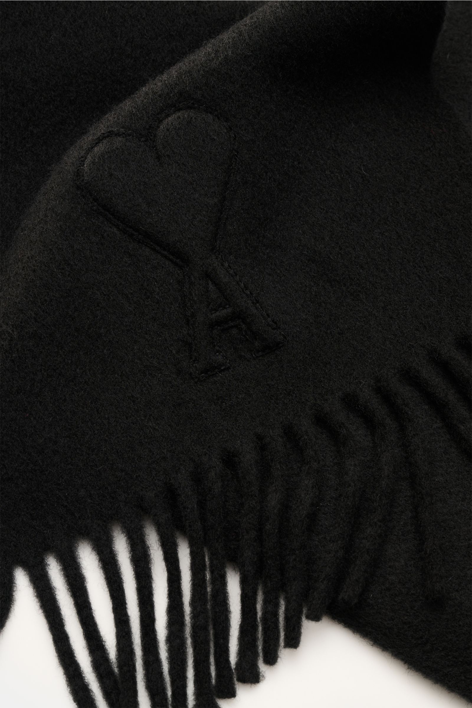 Alt-Tag (124 Zeichen): Nahaufnahme des Ami Paris Schal schwarz aus weicher, gewalkter Wolle mit erhabenem 'Ami de Cœur'-Logo und Fransenkante.