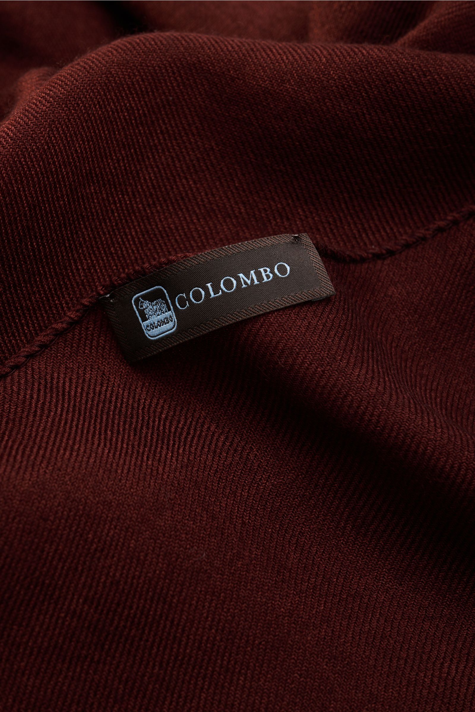 Close-up front view of the Colombo Schal rotbraun showing fabric texture and label, mix of fine cashmere and silk, soft touch, very light quality, rolled edges, narrow fringe edge, dimensions approx. 196 cm x 70 cm.