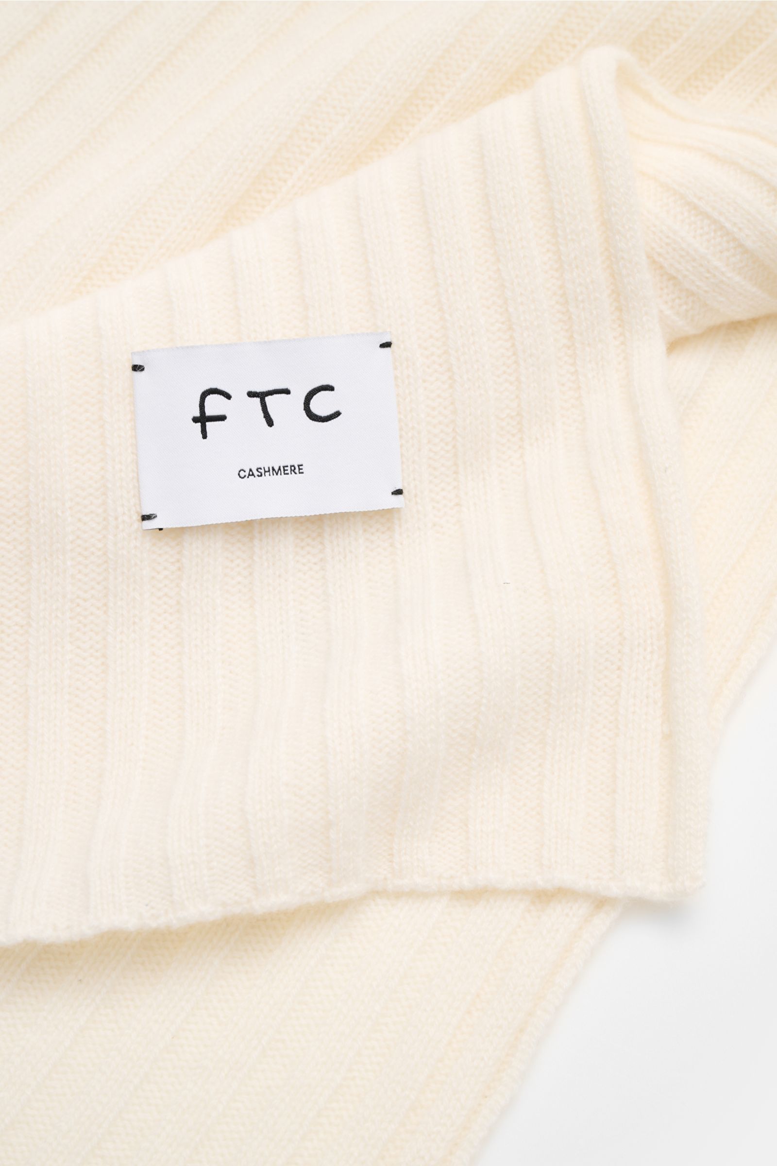 Close-up angled view of the FTC Cashmere scarf cream showing its wide rib knit pattern and large woven logo label.

An elegant, sustainably produced accessory for cold days: This scarf with rib knit pattern by FTC is made of luxurious, pure fair trade 