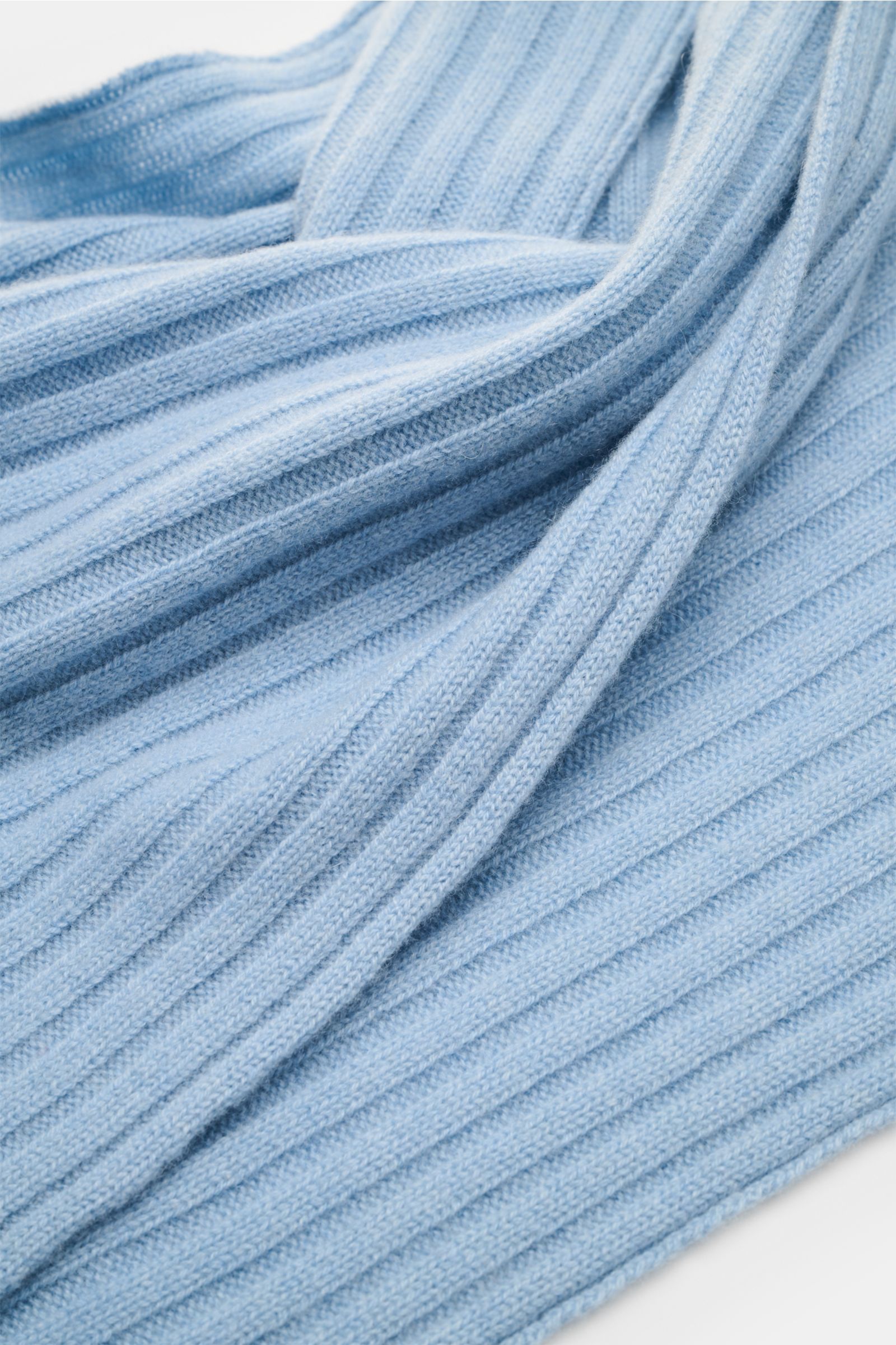Nahaufnahme des FTC Cashmere Schals hellblau mit breitem Rippstrickmuster und weichem Griff, fotografiert aus schräger Perspektive.