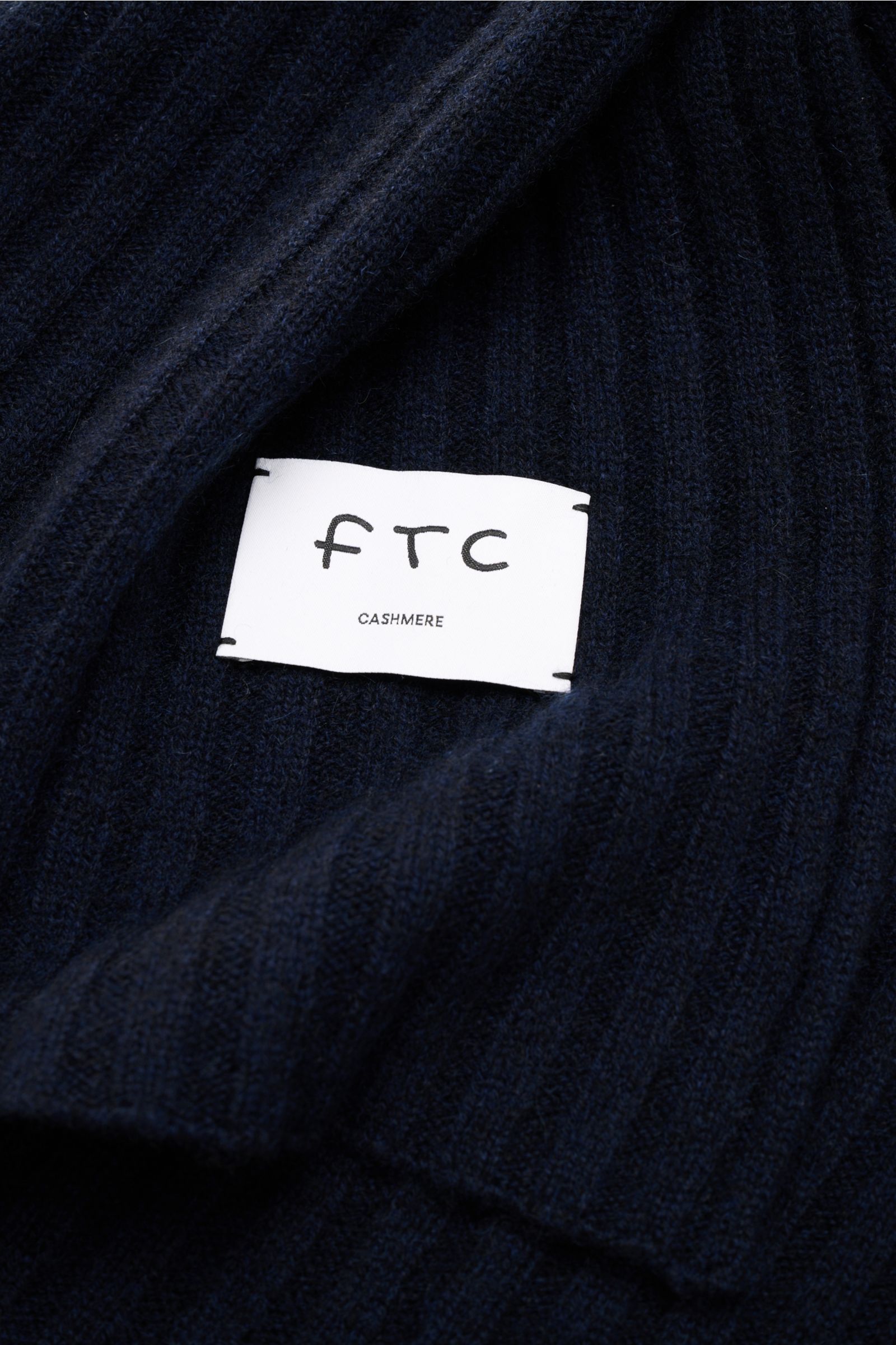 Nahaufnahme des FTC Cashmere Schal navy mit breitem Rippstrickmuster, weichem Griff und sichtbarem weißen Weblabel, nachhaltig aus reinem Fair Trade Cashmere.