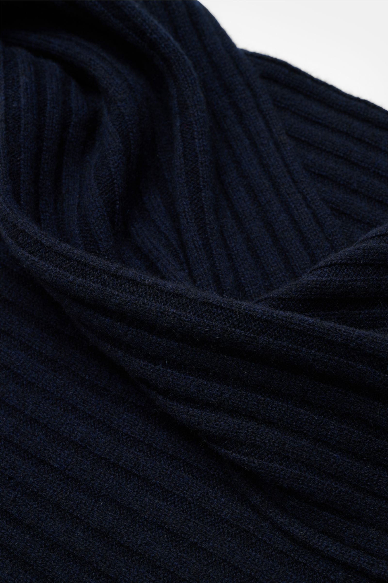 Nahaufnahme des FTC Cashmere Schal navy aus reinem Fair Trade Cashmere mit breitem Rippstrickmuster, weichem Griff und großem Logo-Weblabel, fotografiert aus schräger Draufsicht.