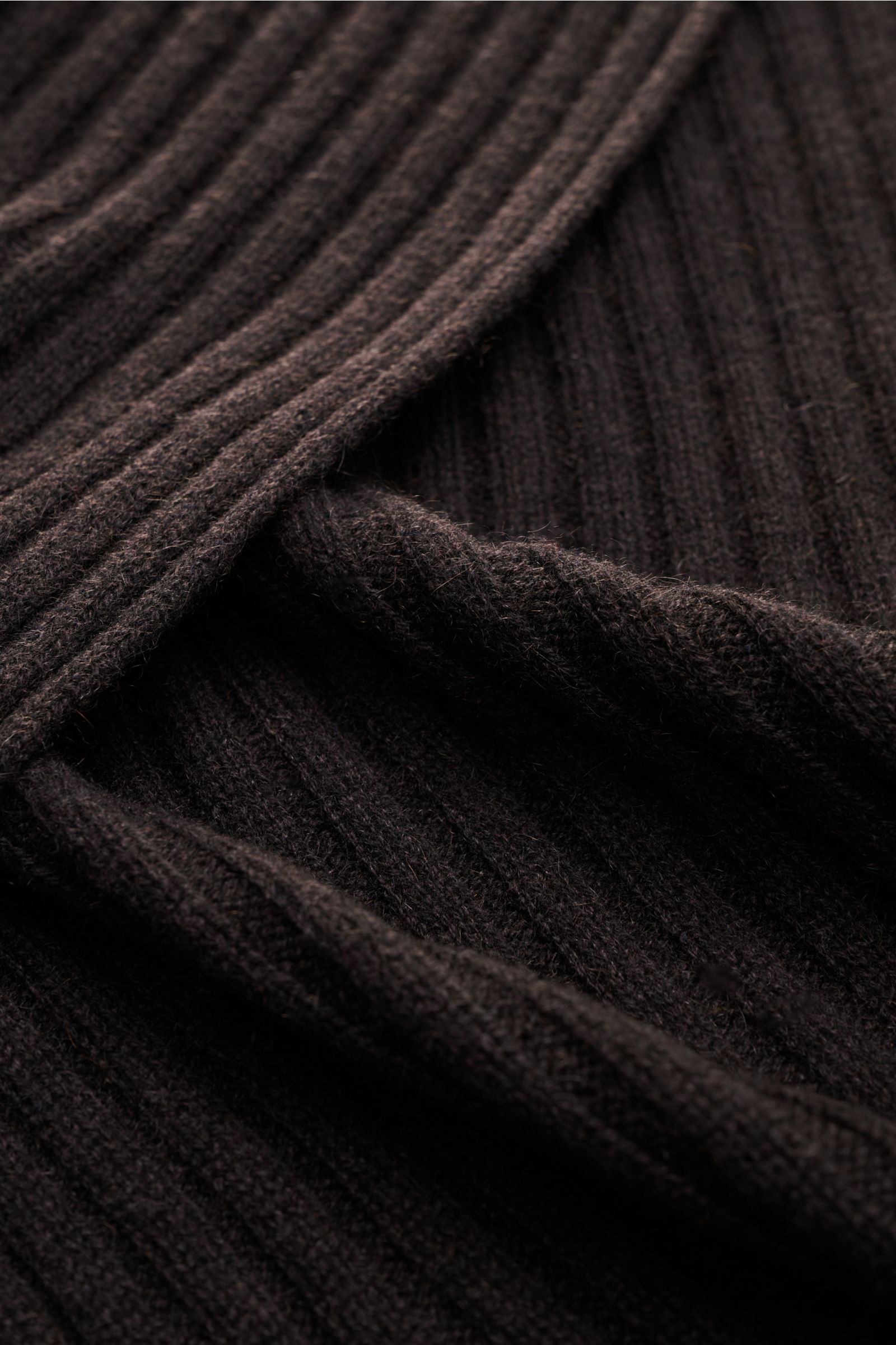Nahaufnahme des FTC Cashmere Schals dunkelbraun mit breitem Rippstrickmuster und weichem Griff, fotografiert aus schräger Perspektive.