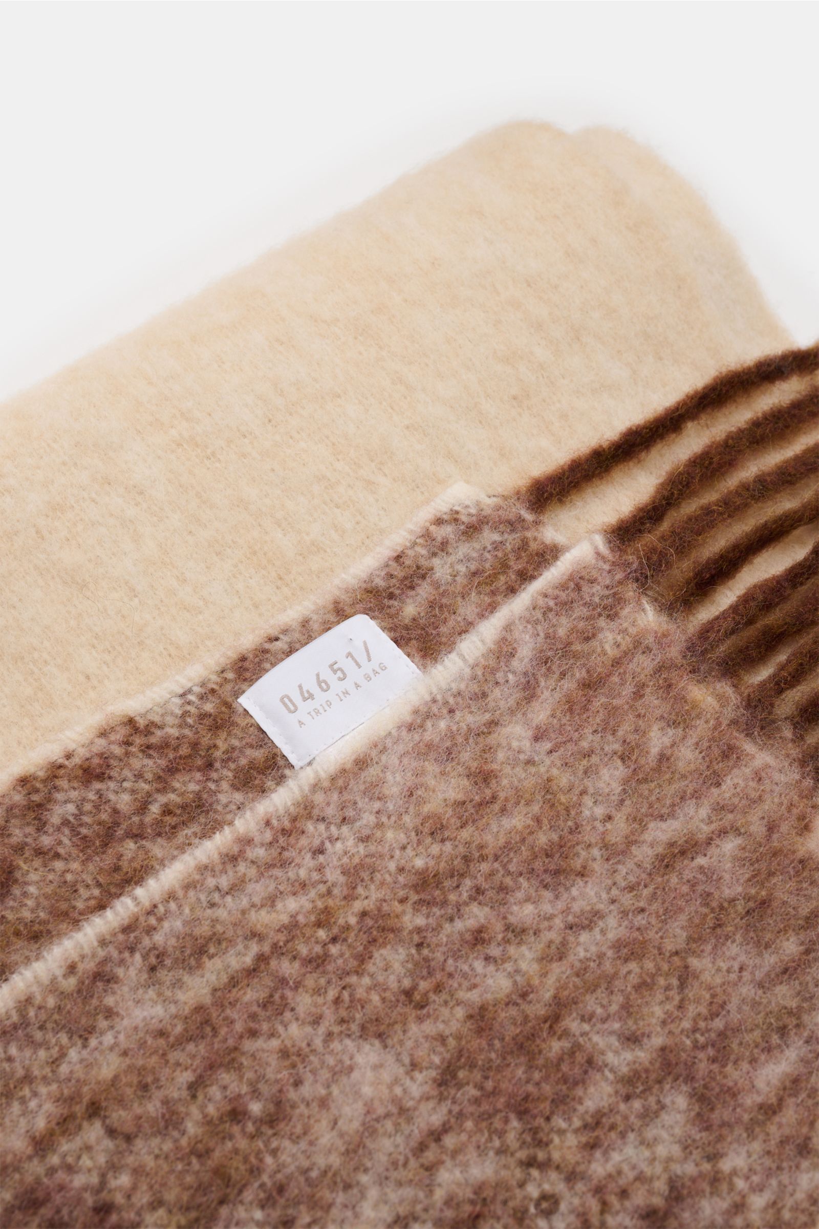 Close-up top view of 04651/ A trip in a bag Schal 'Color Block Scarf' grau/braun/creme showing soft alpaca-wool blend with fringed edge and label.

Additional description: Unverzichtbares Winter-Essential: Der edle Schal von 04651/ A TRIP IN A BAG wird