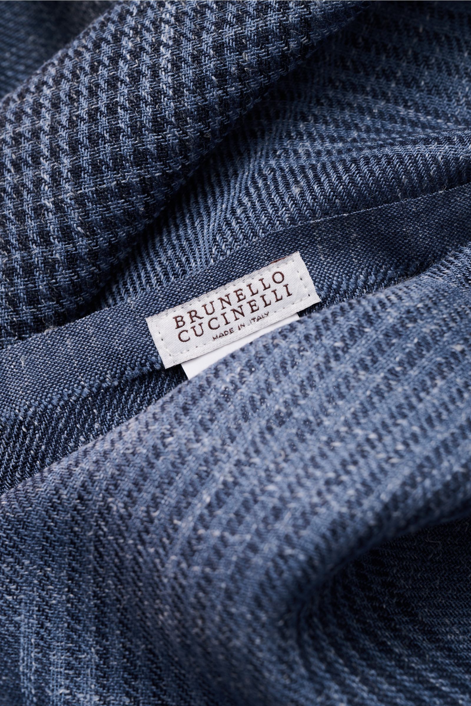 Close-up view of the folded Brunello Cucinelli Schal graublau/navy kariert showing its soft silk and linen blend, lightweight fabric with a check pattern and narrow fringed edge, including the brand label.

Das Quiet-Luxury-Label BRUNELLO CUCINELLI ist