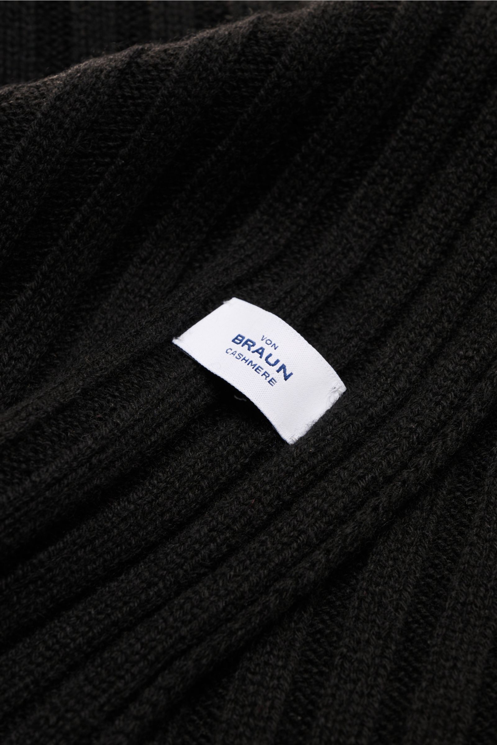 Nahaufnahme des von Braun Cashmere Schals schwarz in klassischem Rippstrick-Design mit feinem Strickbild und weißem Markenlabel, weicher Griff.