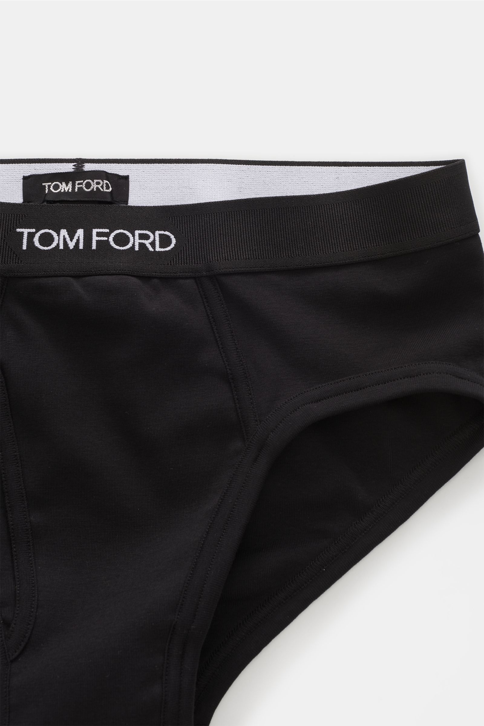 Close-up, top-down view of Tom Ford Sport Slip schwarz, a black men's brief with a wide elastic waistband featuring white TOM FORD stitching, made of soft, elastic cotton with a side fly for comfort.

Description: Auch für drunter setzen wir auf komfor