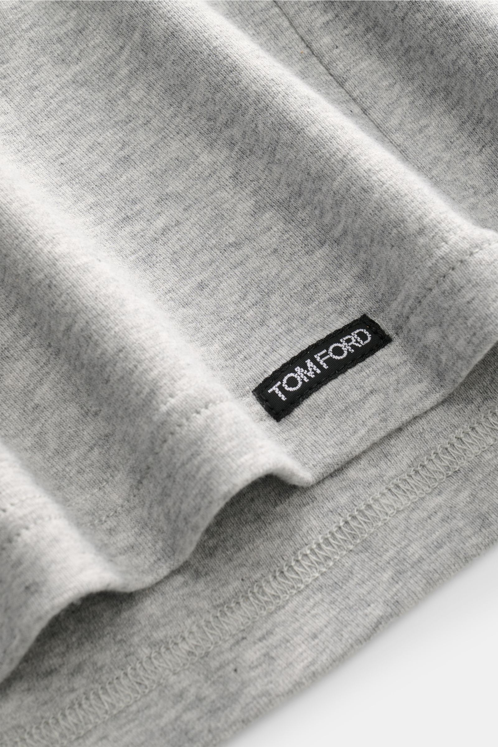 Close-up photo from a side angle of the hem of the Tom Ford V-Neck Unterhemd weiß showing the small black Tom Ford web label, made of jersey aus Baumwolle, komfortabler Stretch-Anteil, sehr weicher Griff, Extra Slim Fit, V-Ausschnitt.