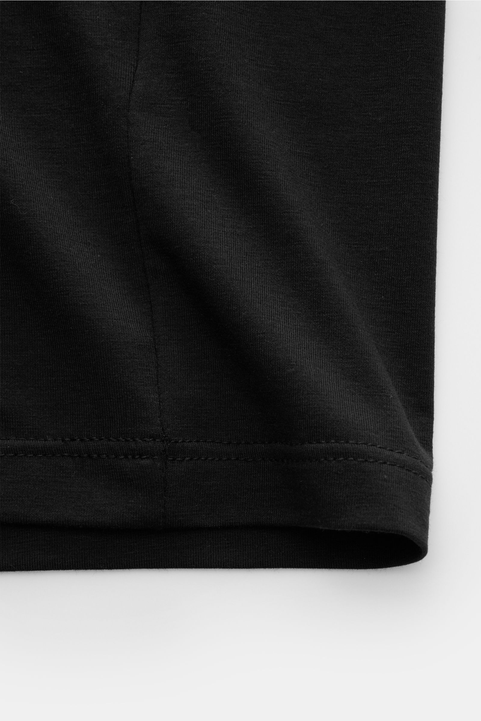 Close-up of the hem detail of the black Tom Ford Rundhals-Unterhemd schwarz, photographed from a side angle. Cleanes Basic mit Rundhalsausschnitt: Das komfortable T-Shirt aus hochwertiger Baumwoll-Modal-Mischung vom Luxus-Label TOM FORD gehört zur Grundau