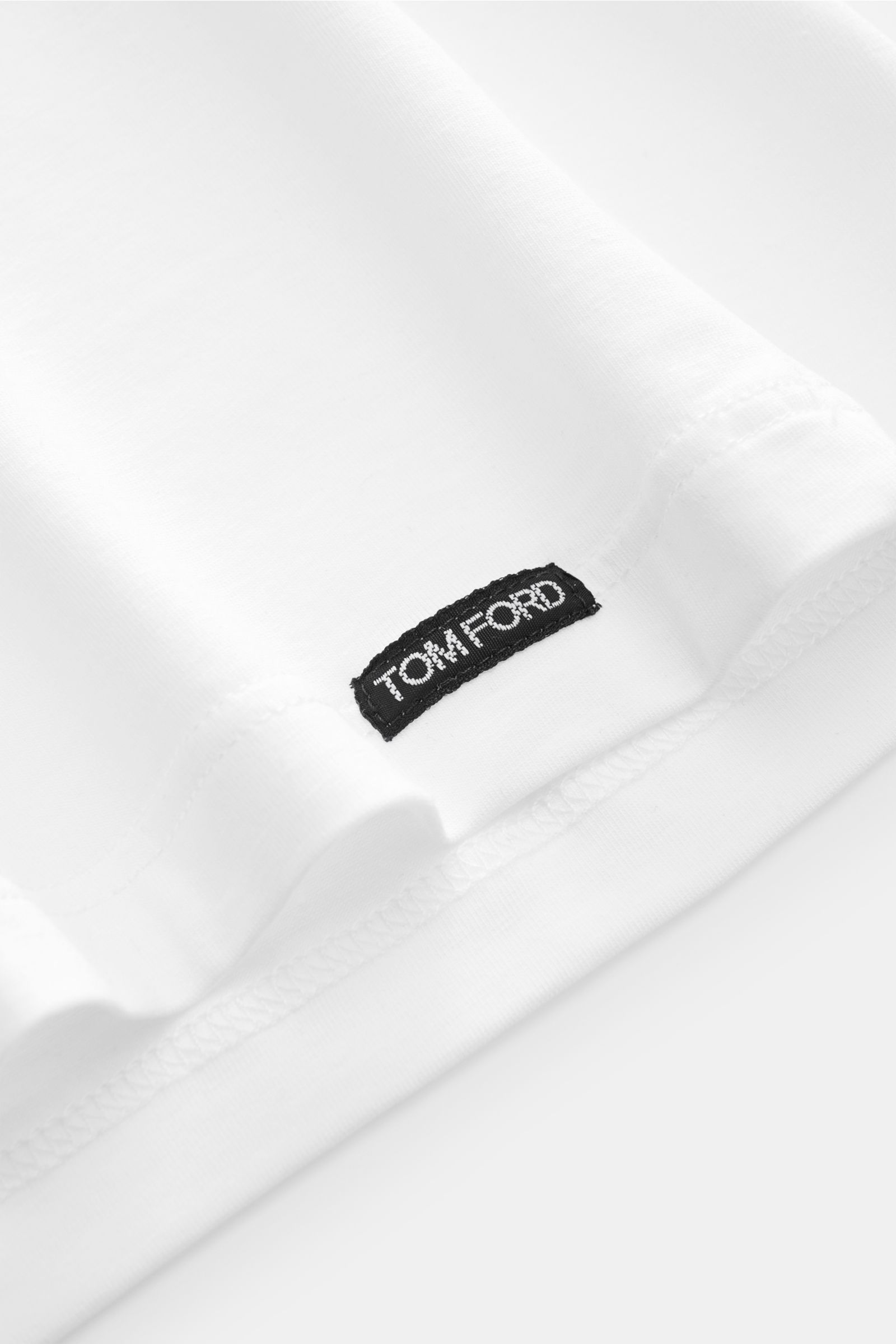 Close-up of the hem of the Tom Ford Rundhals-Unterhemd weiß, showing the small black TOM FORD label on soft, elastic white cotton fabric, photographed from a side angle.

Description: Cleanes Basic mit Rundhalsausschnitt: Das komfortable T-Shirt in hoc