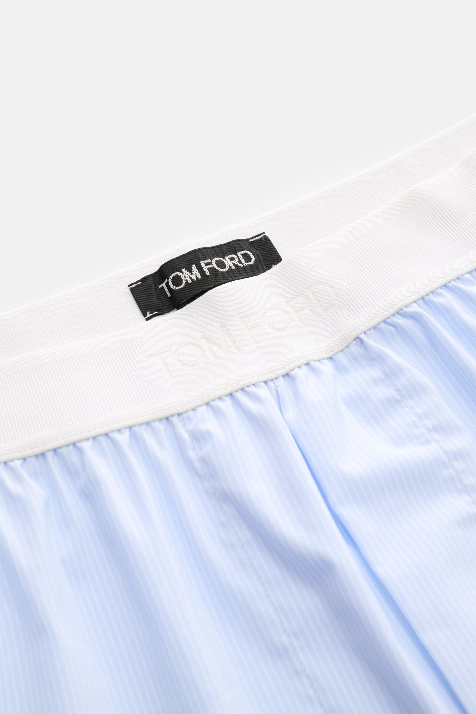 Close-up top view of Tom Ford Boxershorts hellblau/weiß gestreift with elastic white waistband featuring TOM FORD logo, fine stripes, and smooth cotton blend fabric. Sportlich, clean und luxuriös: Diese Boxershorts präsentieren sich im feinen Streifenmust