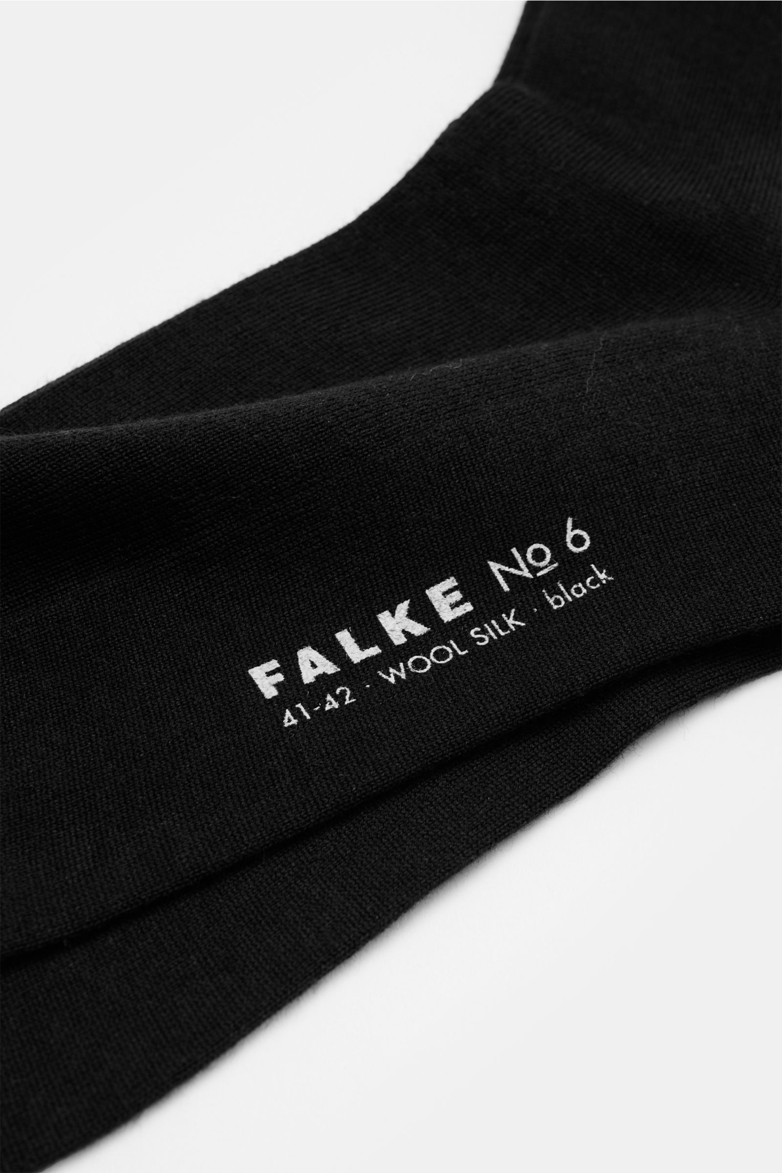 Black Falke Strumpf 'No. 7' schwarz sock laid flat, close-up from side angle showing texture and white brand text. Optimale Passform, luxuriöse Materialqualität, FALKE: Der Strumpf 'No. 7' des Traditionslabels garantiert durch feinste two-ply Merinowol