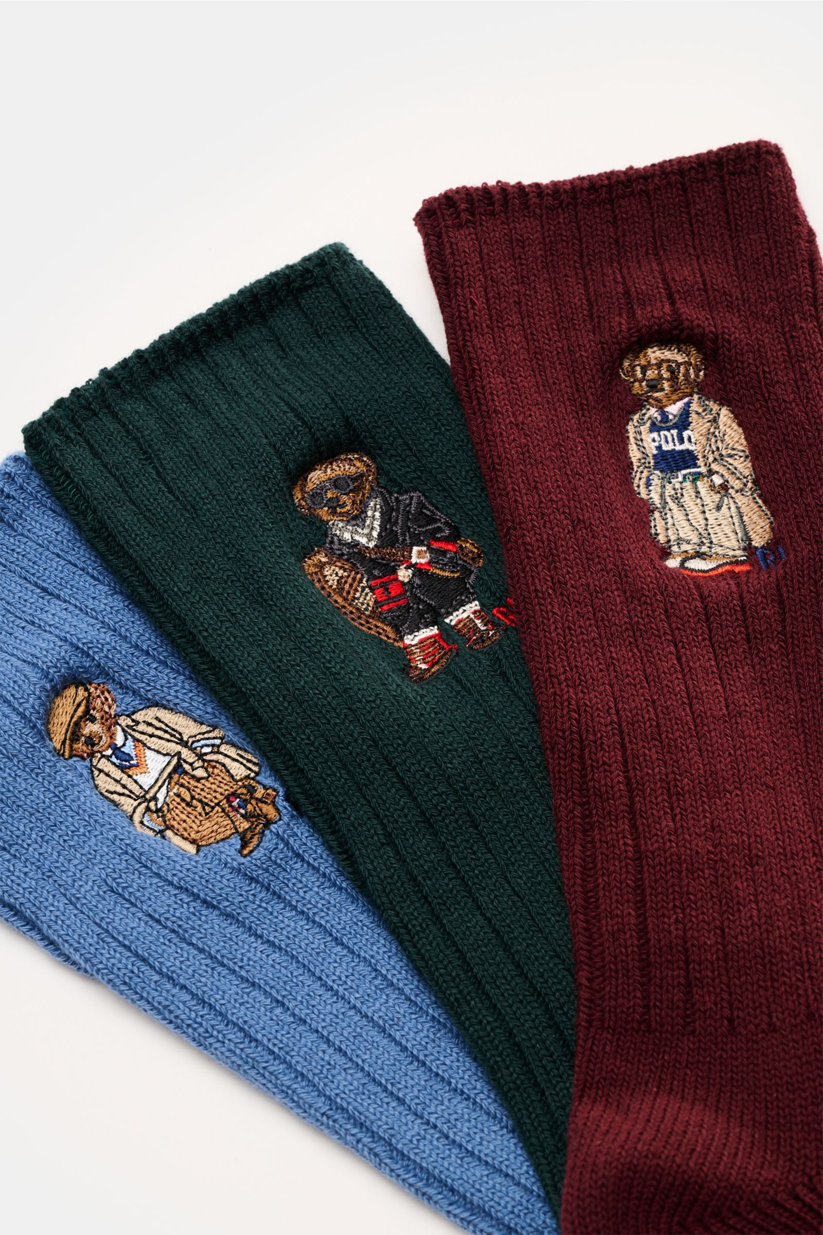Top-down view of Polo Ralph Lauren Strümpfe 3er-Set rauchblau/dunkelgrün/bordeaux ribbed socks with embroidered teddy designs.

Stylishe Statements für die kalte Jahreszeit: Die Strümpfe mit dem charakteristischen POLO RALPH LAUREN Teddy-Stitching setz
