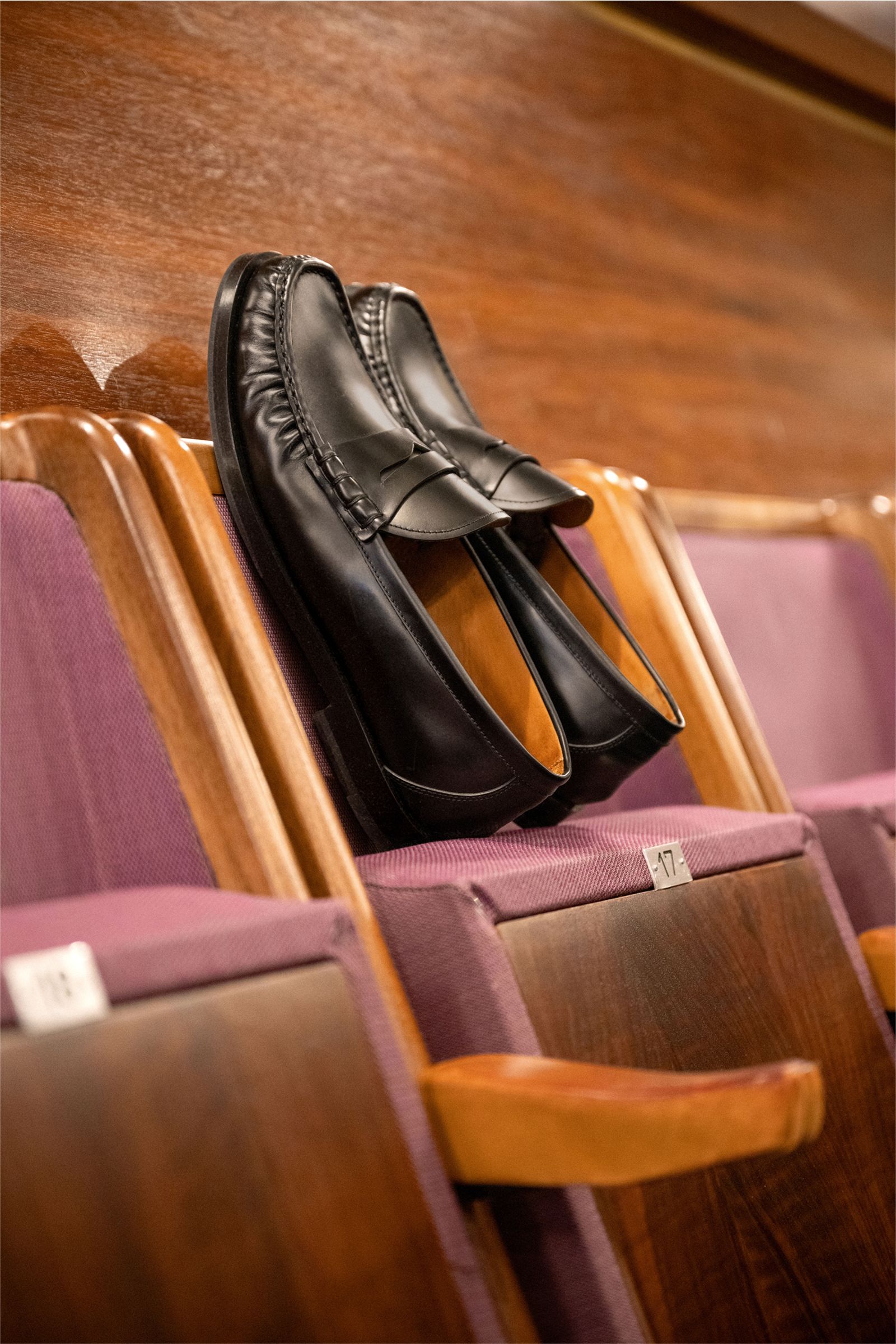 Officine Creative Penny Loafer 'Balfron' schwarz aus poliertem Glattleder, schmal zulaufend, mit Penny Strap, Zierfalten, Lederfutter, Gummisohle, seitlich auf Theaterstuhl.