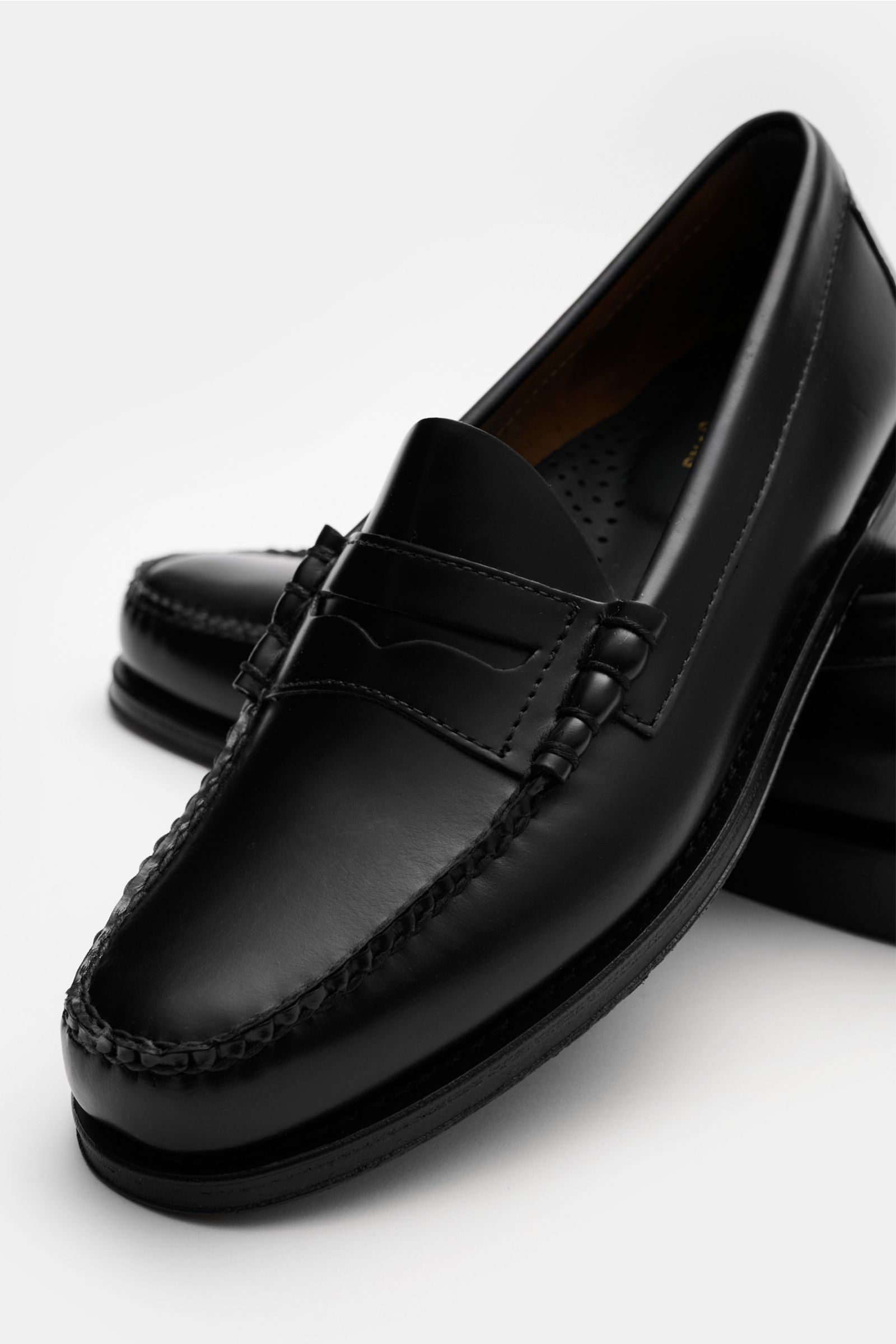 G.H.Bass Penny Loafer 'Weejuns Larson' schwarz in black leather, photographed from front-side angle, smooth leather, penny strap, moc toe, stitched construction, leather lining, cushioned footbed, leather sole, rubber heel, decorative lacing.