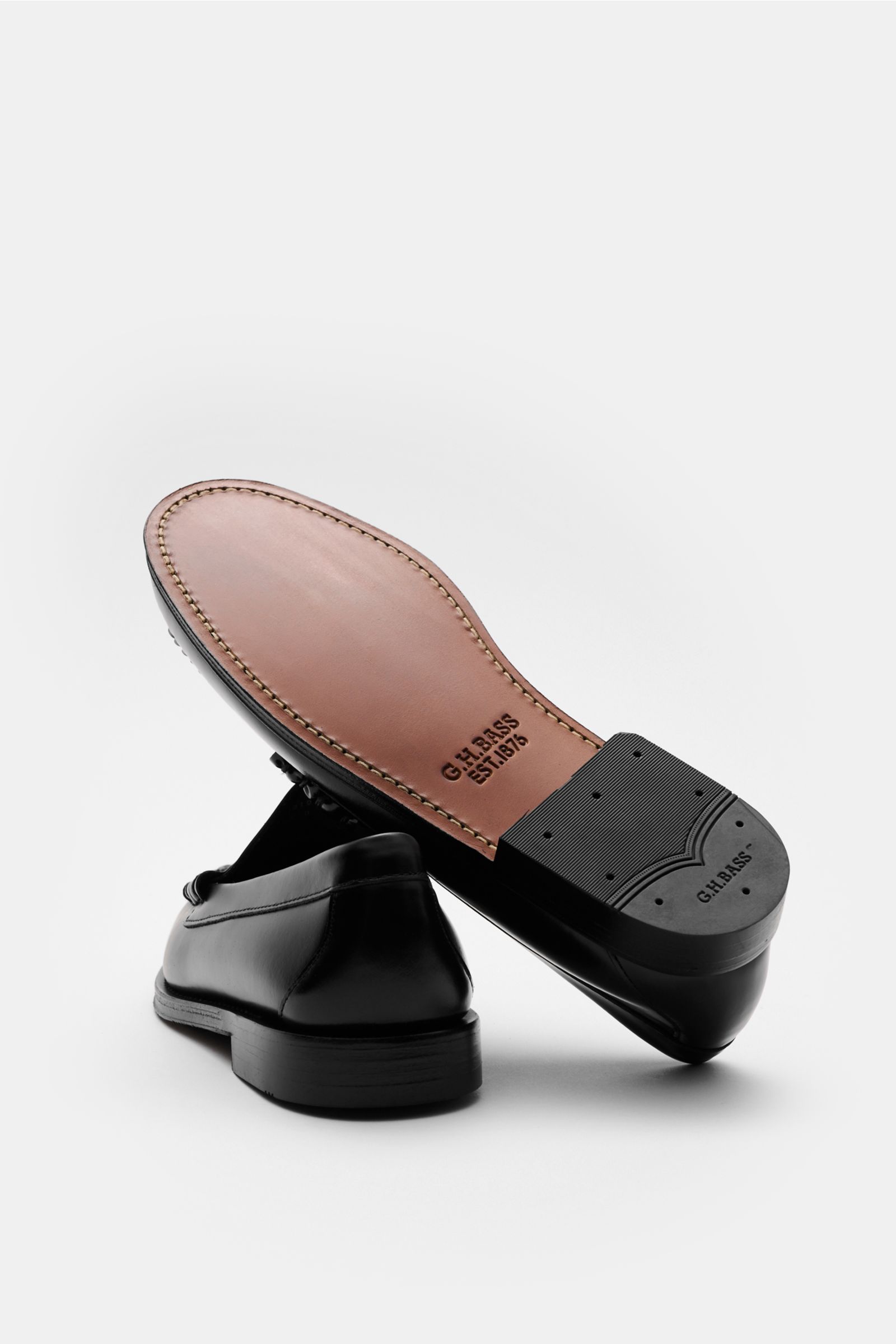 G.H.Bass Penny Loafer 'Weejuns Larson' schwarz shown from a low rear angle with one shoe upright and the other tilted to display the leather sole and rubber-reinforced heel, featuring smooth black leather, penny strap, decorative stitching, leather lining