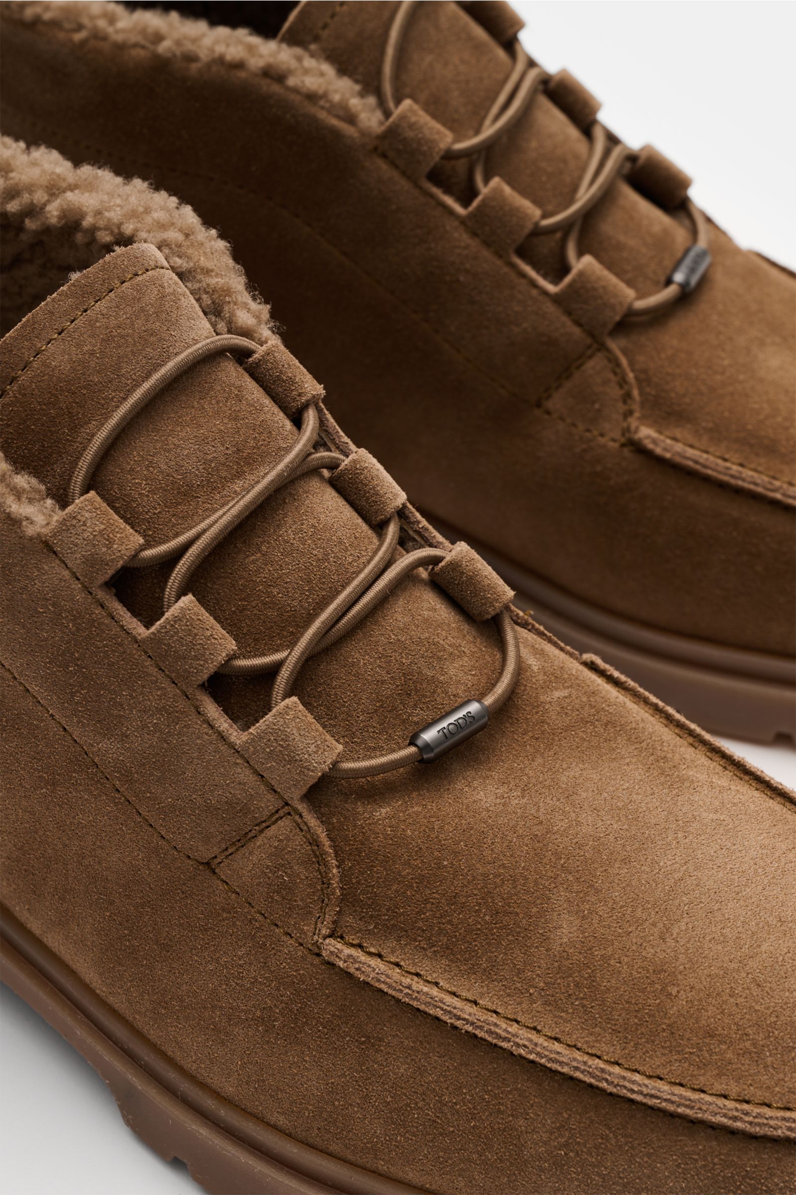 Nahaufnahme von Tod's Boot graubraun aus edlem Veloursleder mit Lammfell-Futter, elastischer Schnürung und genoppter Sohle, seitliche Perspektive.