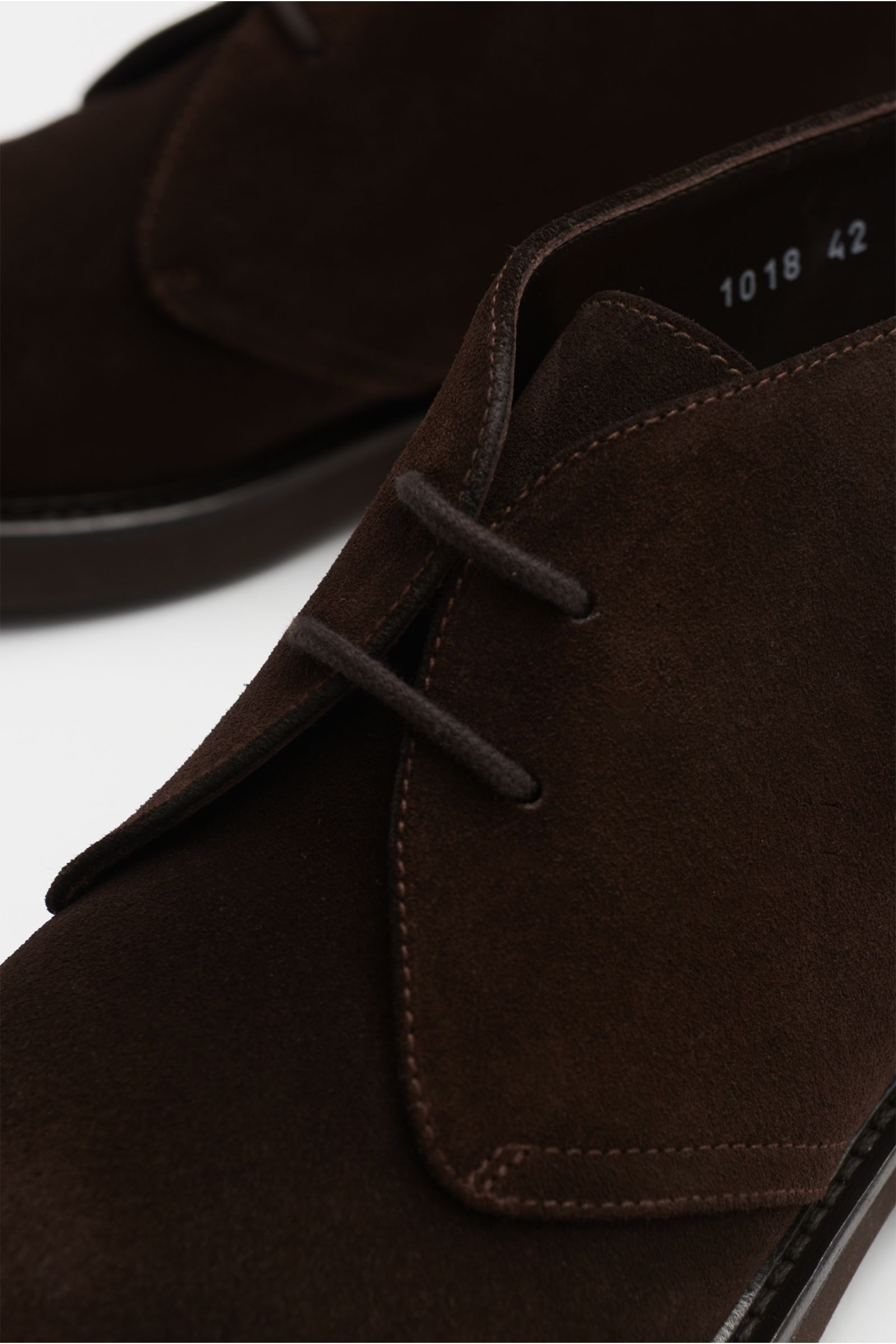 Close-up front-side view of Doucal's Desert boots dark brown in fine suede, featuring a tapered silhouette, two-eyelet lacing, leather lining, and rubber outsole.