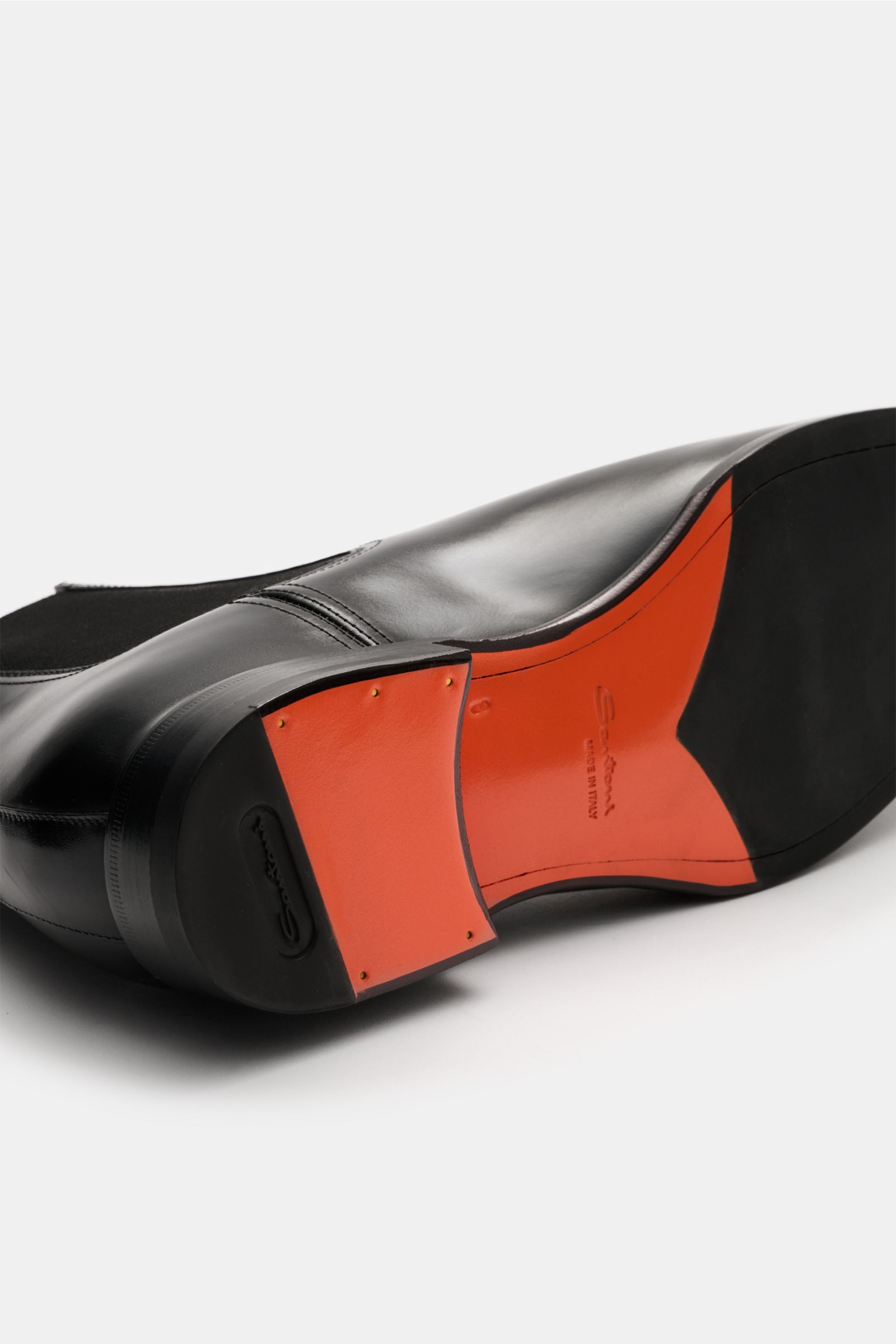 Santoni Chelsea Boot 'Adrian' schwarz shown from a low rear-side perspective highlighting smooth black leather, sleek silhouette, and red sole. Ein Klassiker – zeitlos und elegant: Der Chelsea Boot 'Adrian' von SANTONI vereint hochwertiges Glattleder mit 