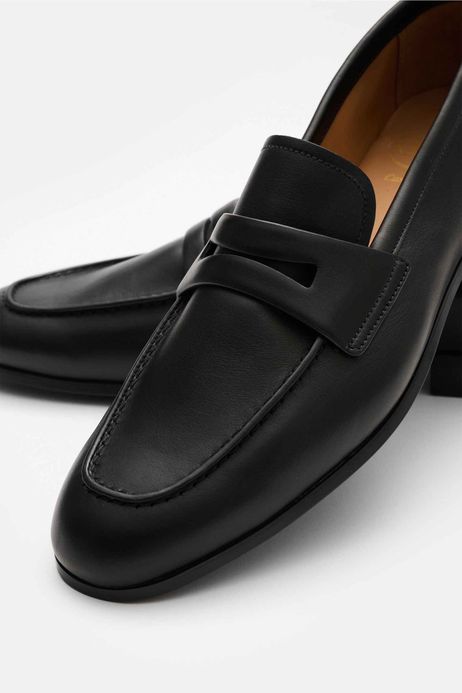Church's Penny Loafer 'Milton' schwarz, schmal zulaufend, aus geschmeidigem Glattleder, mit Penny-Strap und umlaufender Ziernaht, von schräg vorne.