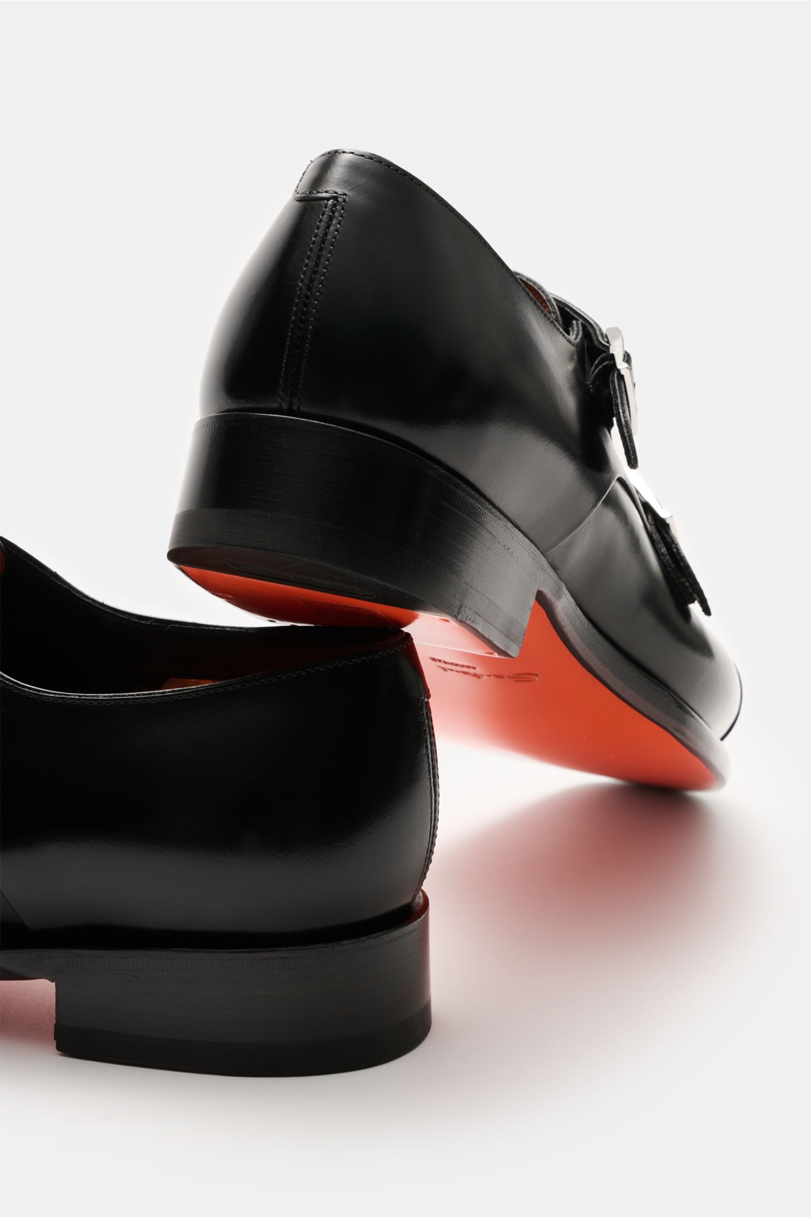 Santoni Doppelmonk schwarz shoes shown from a low rear angle, featuring elegant black calf leather, rounded front cap, overlay cross cap, silver buckles, leather lining, leather sole, and rubber-reinforced heel. Edle Handarbeit wird bei diesem eleganten D
