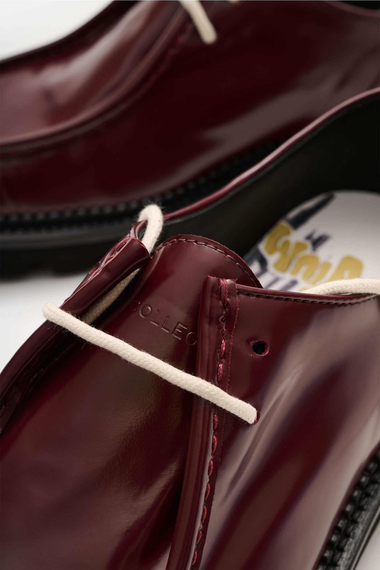 Nahaufnahme des Collegium Derby 'Pillar Moc-Toe' bordeaux aus schräger Perspektive, glänzendes glattes Leder, schmal zulaufende Silhouette, offene Zwei-Loch-Schnürung, Ziernaht auf der Kappe, ledernes Innenfutter, profilierte Gummisohle.