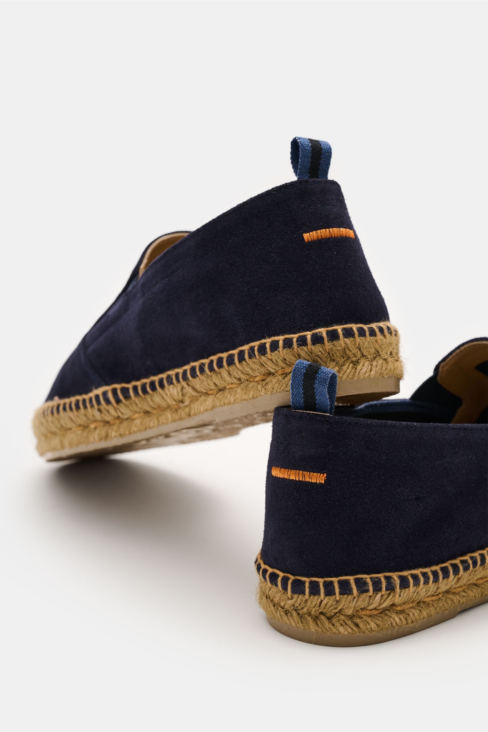 Pair of Castañer Espadrilles 'Joel' navy photographed from a low rear angle, showing navy veloursleder with soft grip, slightly tapered shape, side elastic inserts, practical pull tabs, decorative orange stitching on the heel, braided jute trim, and flexi