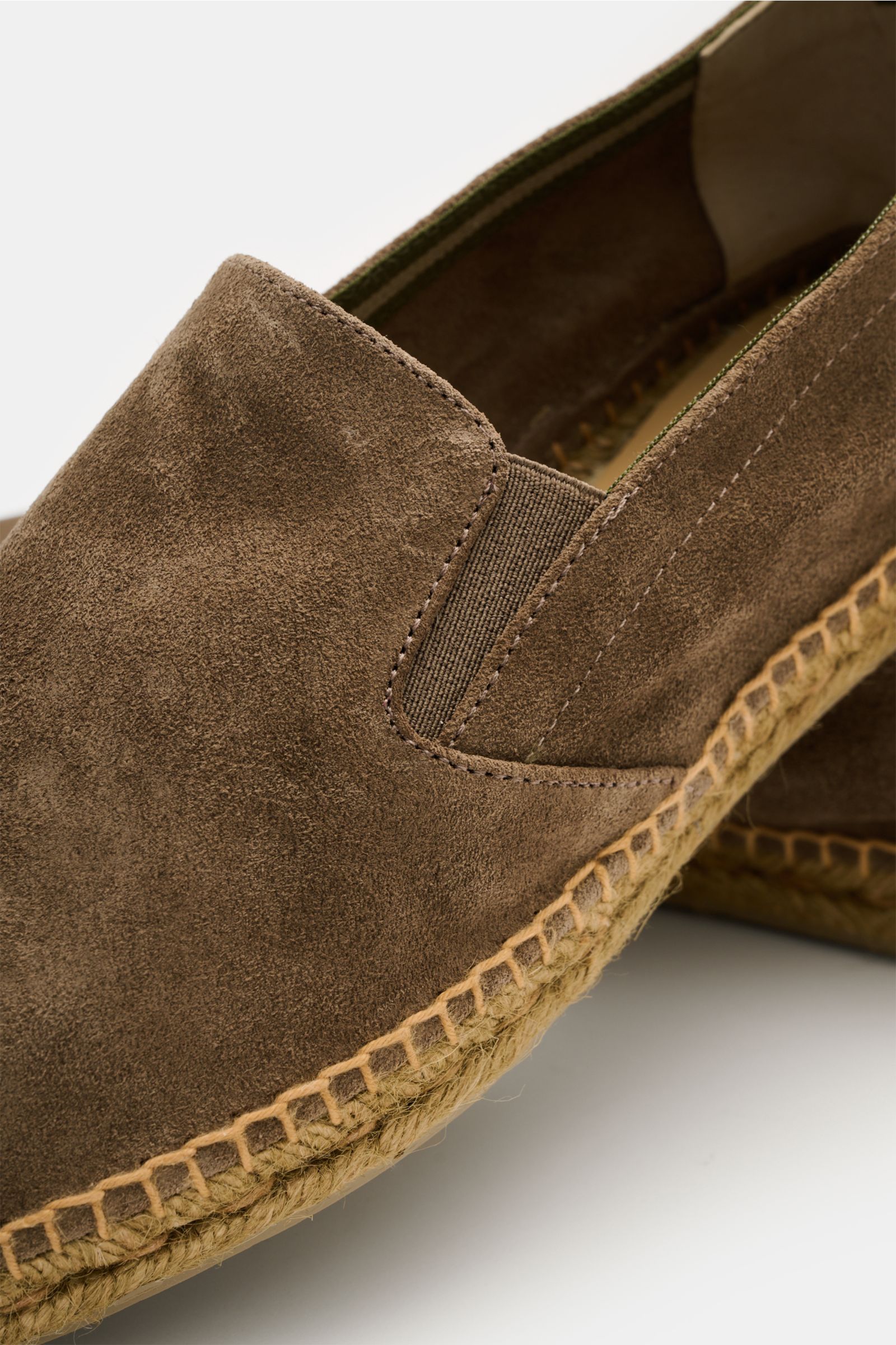 Close-up, angled view of Castañer Espadrilles 'Joel' taupe made from smooth suede with soft grip, narrow taper, side elastic inserts, practical pull loop, decorative rear stitching, jute braided trim, and flexible rubber sole. Legerer Klassiker: Mit diese