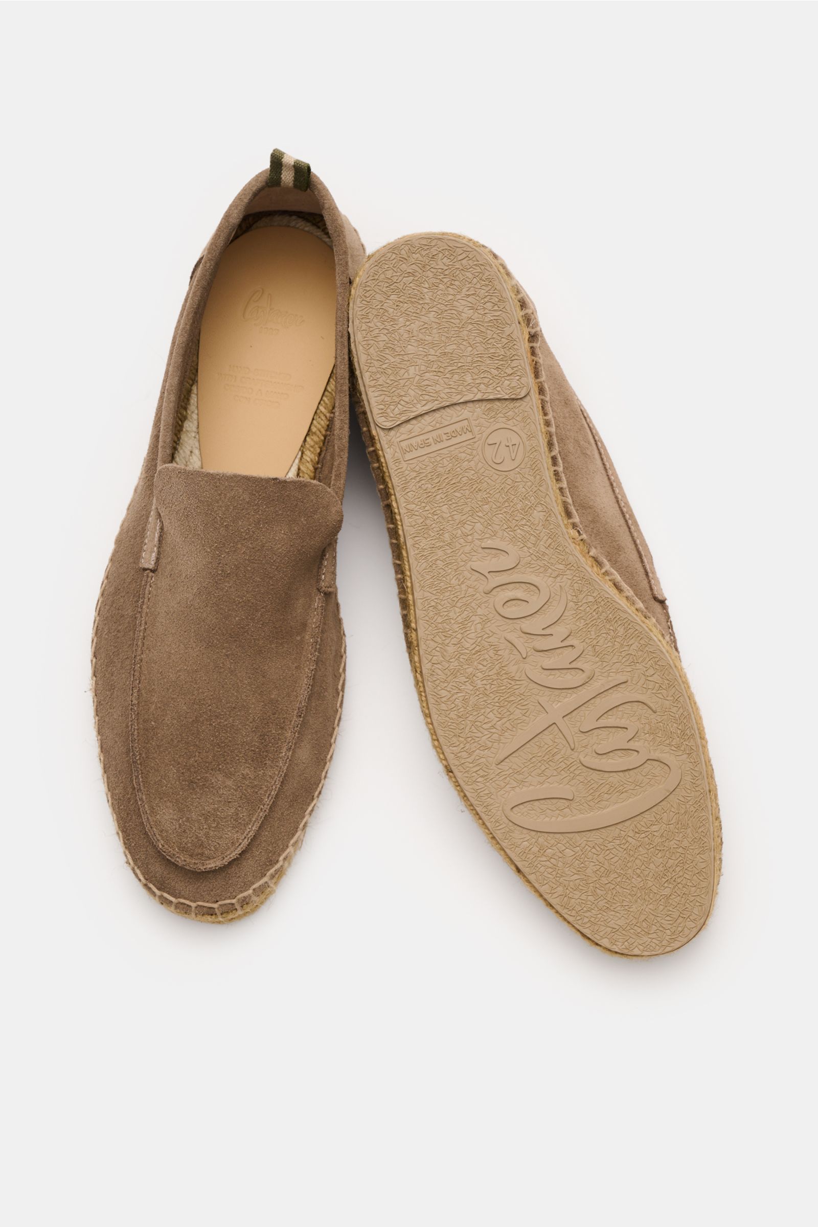 Top-down view of Castañer Espadrilles 'Nino T' taupe in soft suede, showing one shoe’s upper with a slightly tapered cut and decorative toe seam, and the other shoe’s sole featuring braided jute edging and flexible natural rubber sole with logo. Summery l