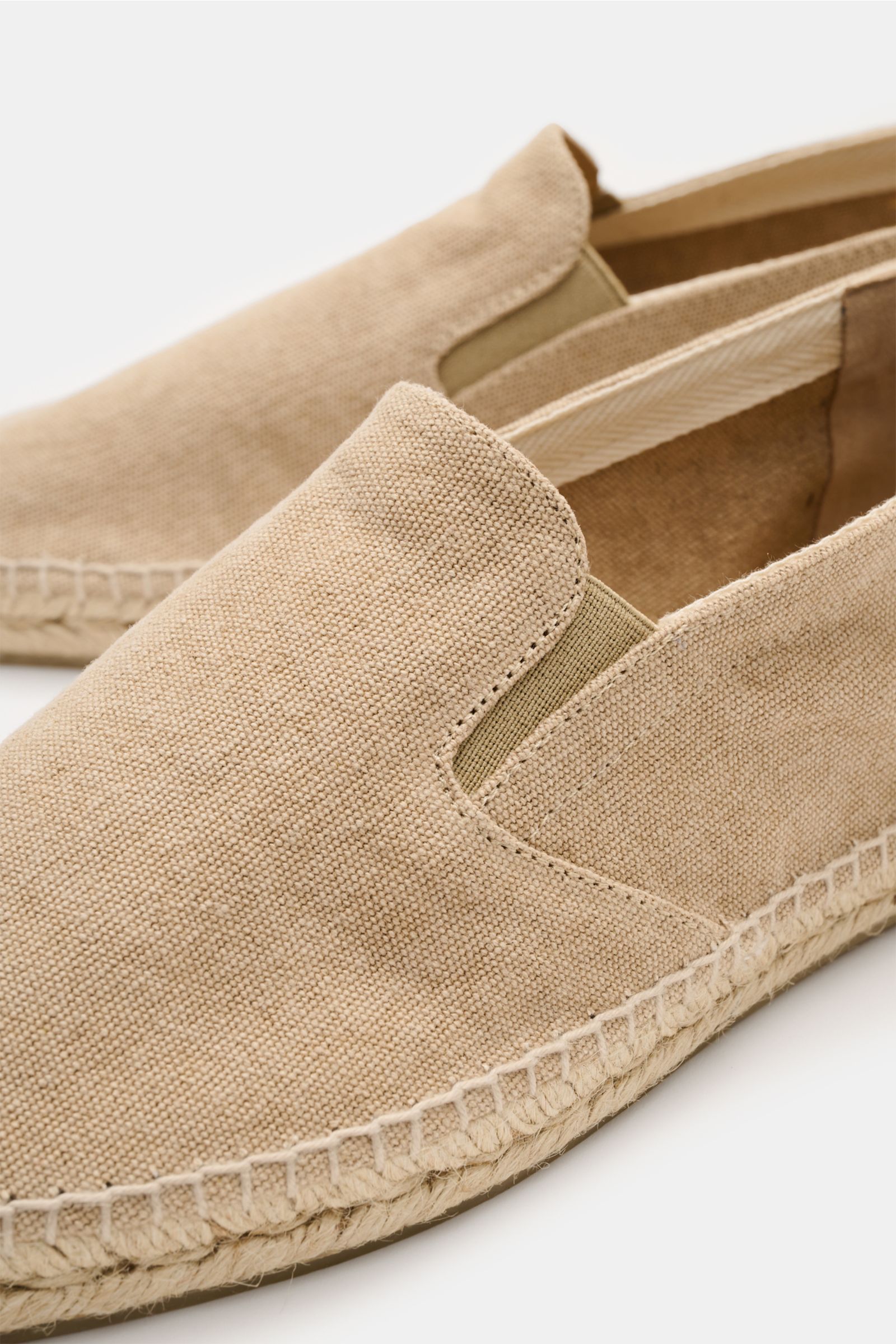 Castañer Espadrilles 'Joel' beige shown from a close-up side angle, featuring canvas cotton, elastic inserts, jute trim, and flexible rubber sole. Die Espadrilles 'Joel' von CASTAÑER aus Canvas verbinden gekonnt die markentypische vulkanisierte Gummiso