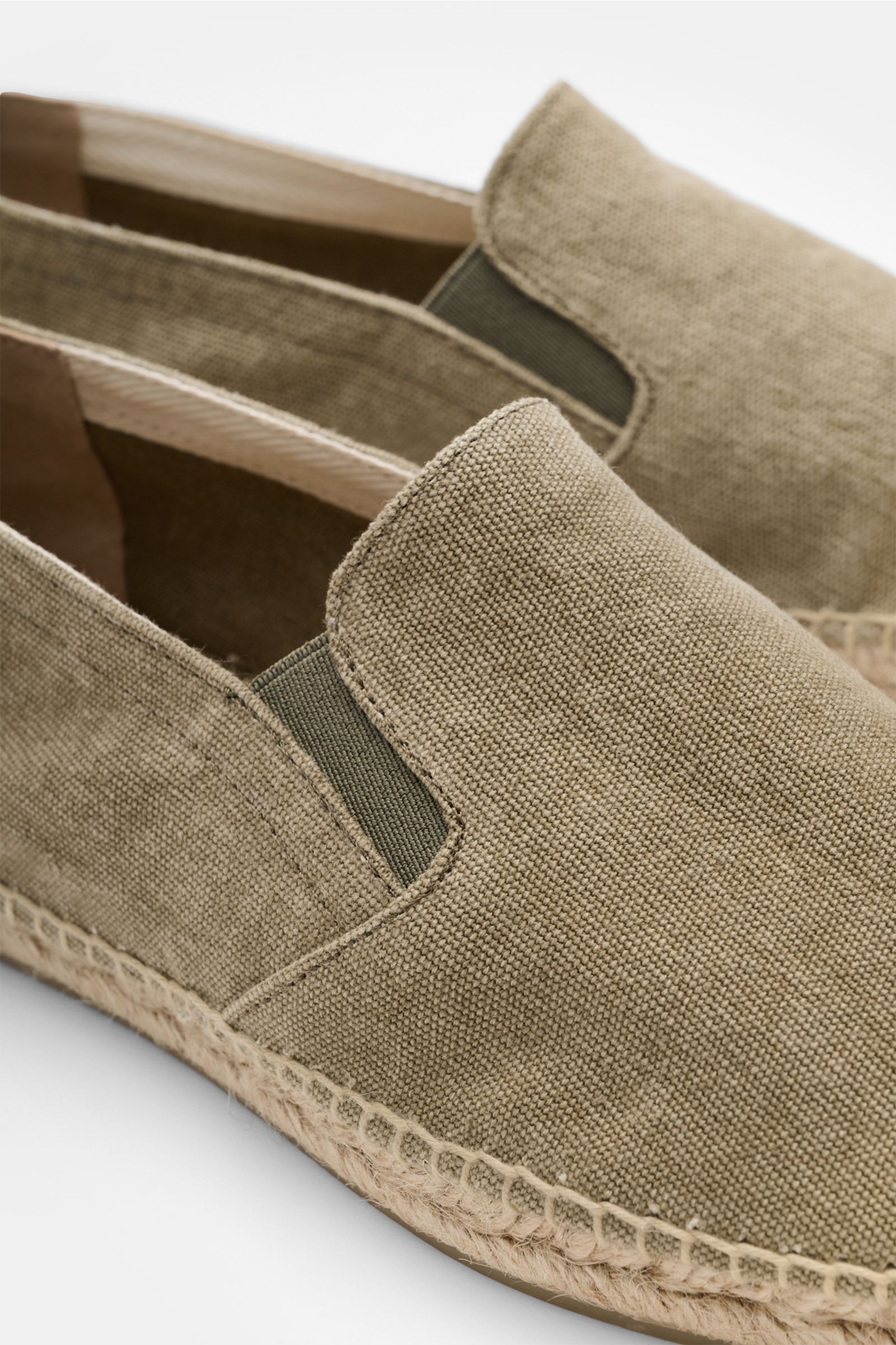 Close-up front-side view of Castañer Espadrilles 'Joel' taupe in cotton canvas with elastic inserts, jute trim, decorative back stitching, and flexible rubber sole.
