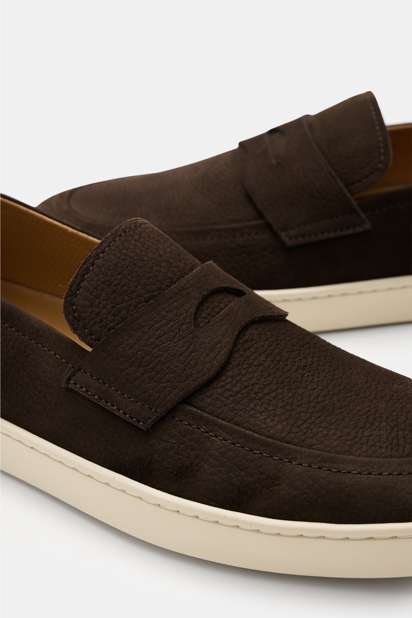 Henderson Penny Loafer 'Mentone' dunkelbraun aus geschmeidigem Nubukleder, schmal zulaufend, mit Penny-Strap, Ziernaht, Lederfutter, Logo-Stitching, flexibler Gummisohle, seitliche Nahaufnahme.