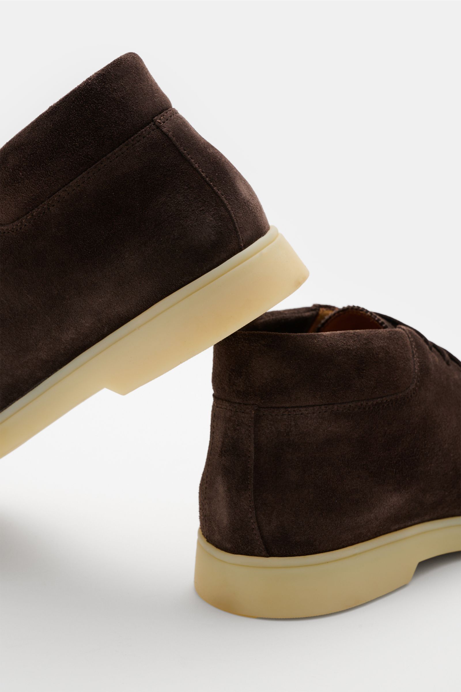 Rear and side view of Aurélien Desert Boot dunkelbraun in smooth dark brown suede with light cream flexible rubber sole, padded collar, and distinctive front cap seam, photographed close-up showcasing the elegant, slightly tapered silhouette and open thre