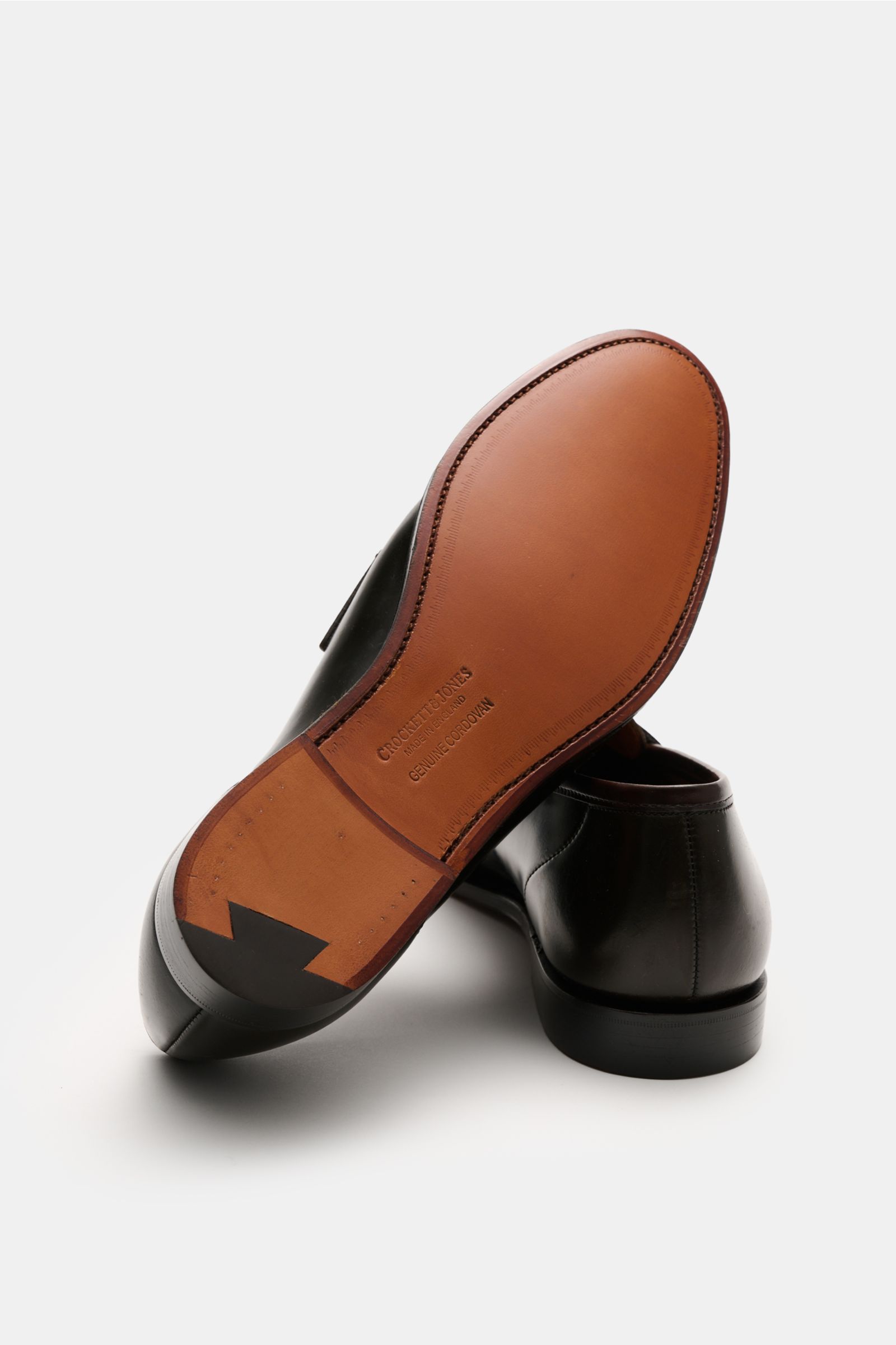 Crockett & Jones Penny Loafer 'Harvard' dunkelbraun aus poliertem Glattleder mit schmaler Silhouette, Penny Strap und Lederlaufsohle, von unten fotografiert.