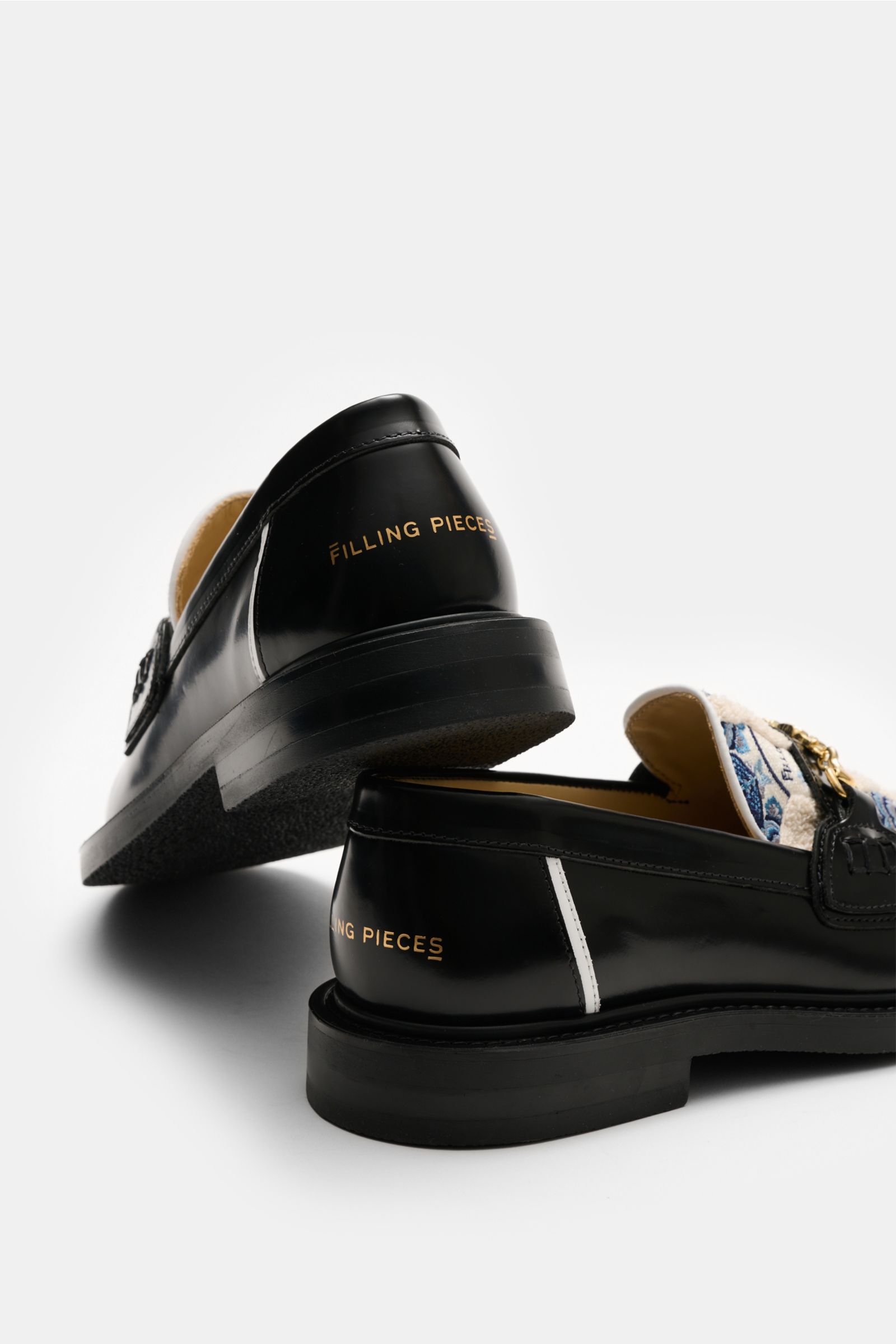 Rear angled view of Filling Pieces Loafer 'Broken Plate' schwarz/blau/offwhite with polished smooth leather, microfiber patch, slim silhouette, handshake bridge buckle, leather lining, and rubber sole, featuring intricate Amsterdam canal drawings on a cla