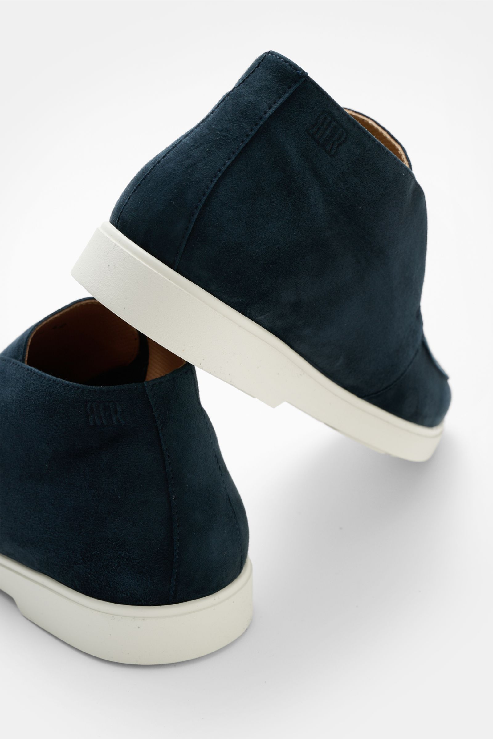 Detailaufnahme von zwei Fabiano Ricci Desert Boot 'Reverse' navy Schuhen aus edlem Veloursleder, schmal zulaufender Silhouette, Naht auf der Vorderkappe, Innenfutter aus Leder und flexibler weißer Gummisohle, fotografiert von hinten schräg oben.